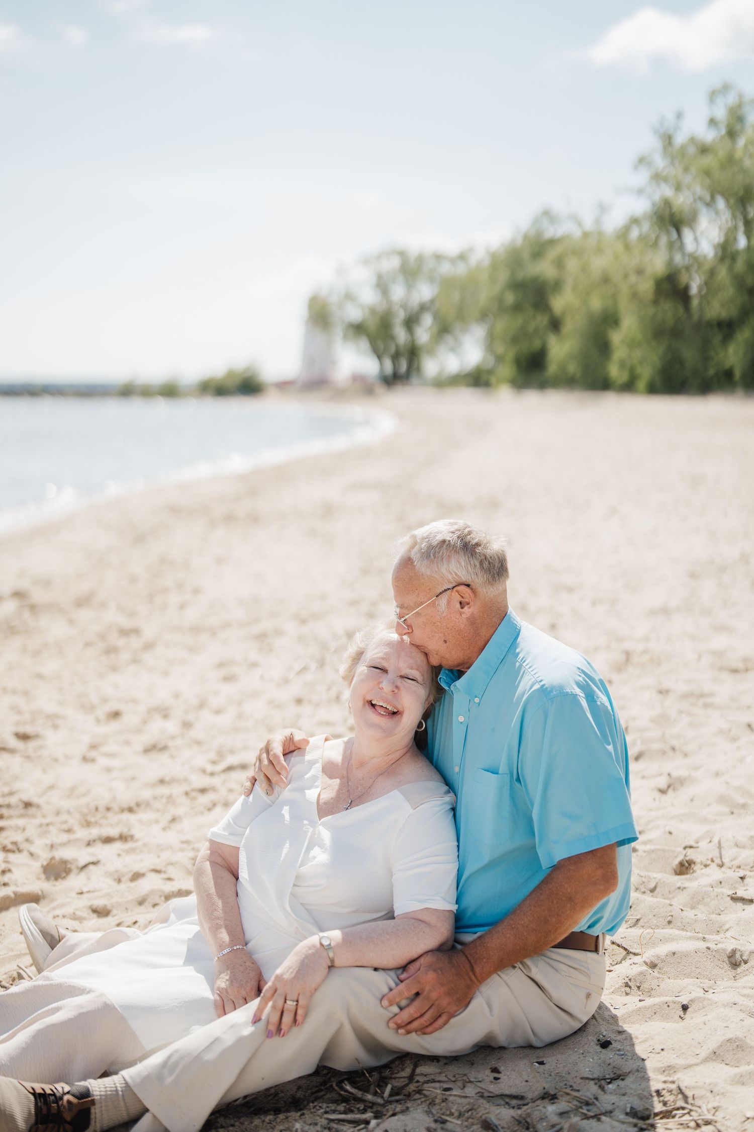 Couple in white and turquoise outfits sharing tender moments together while relaxing on a sandy beach.