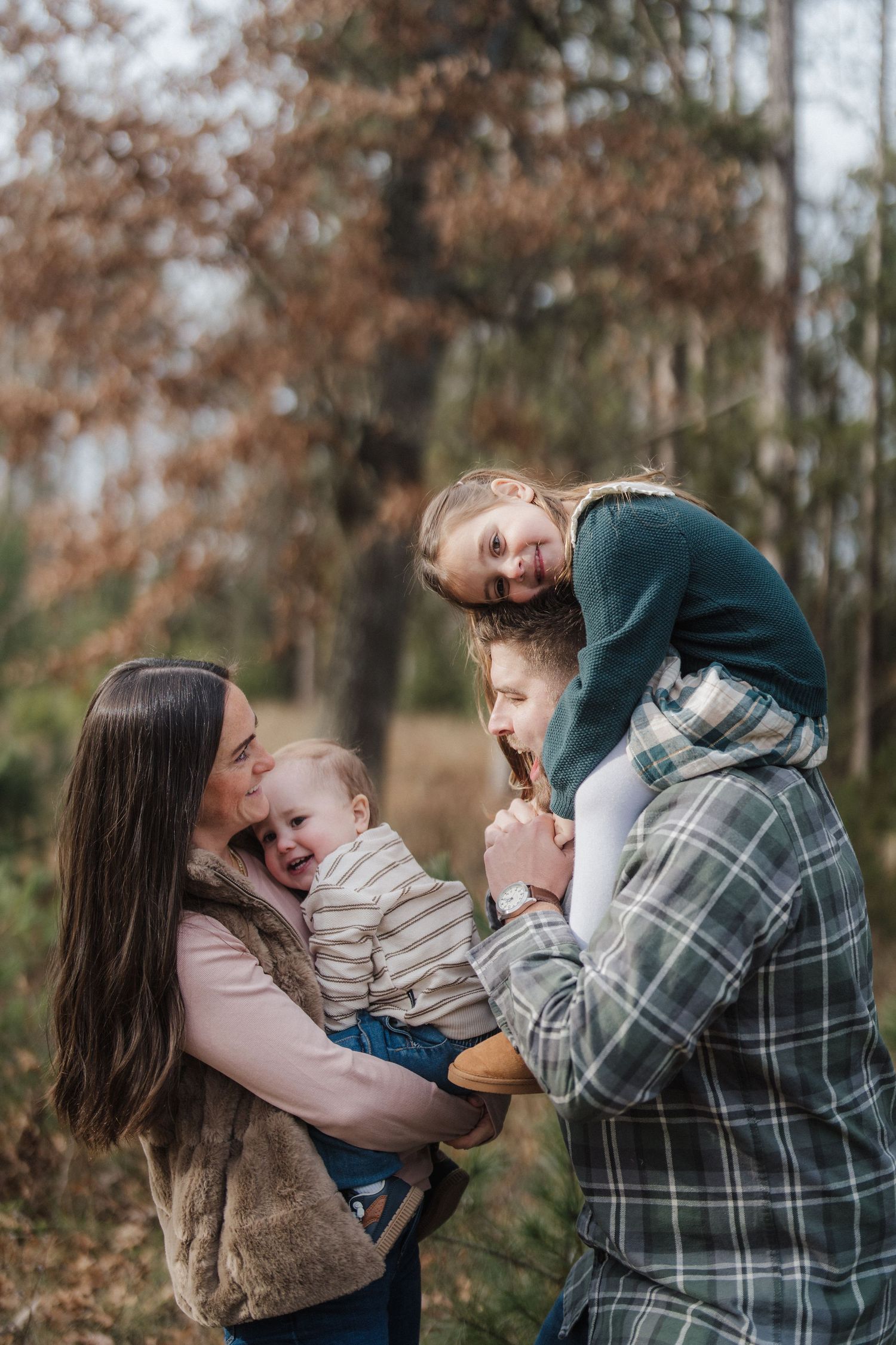 A family shares joyful moments together during an outdoor autumn photoshoot in a wooded setting.