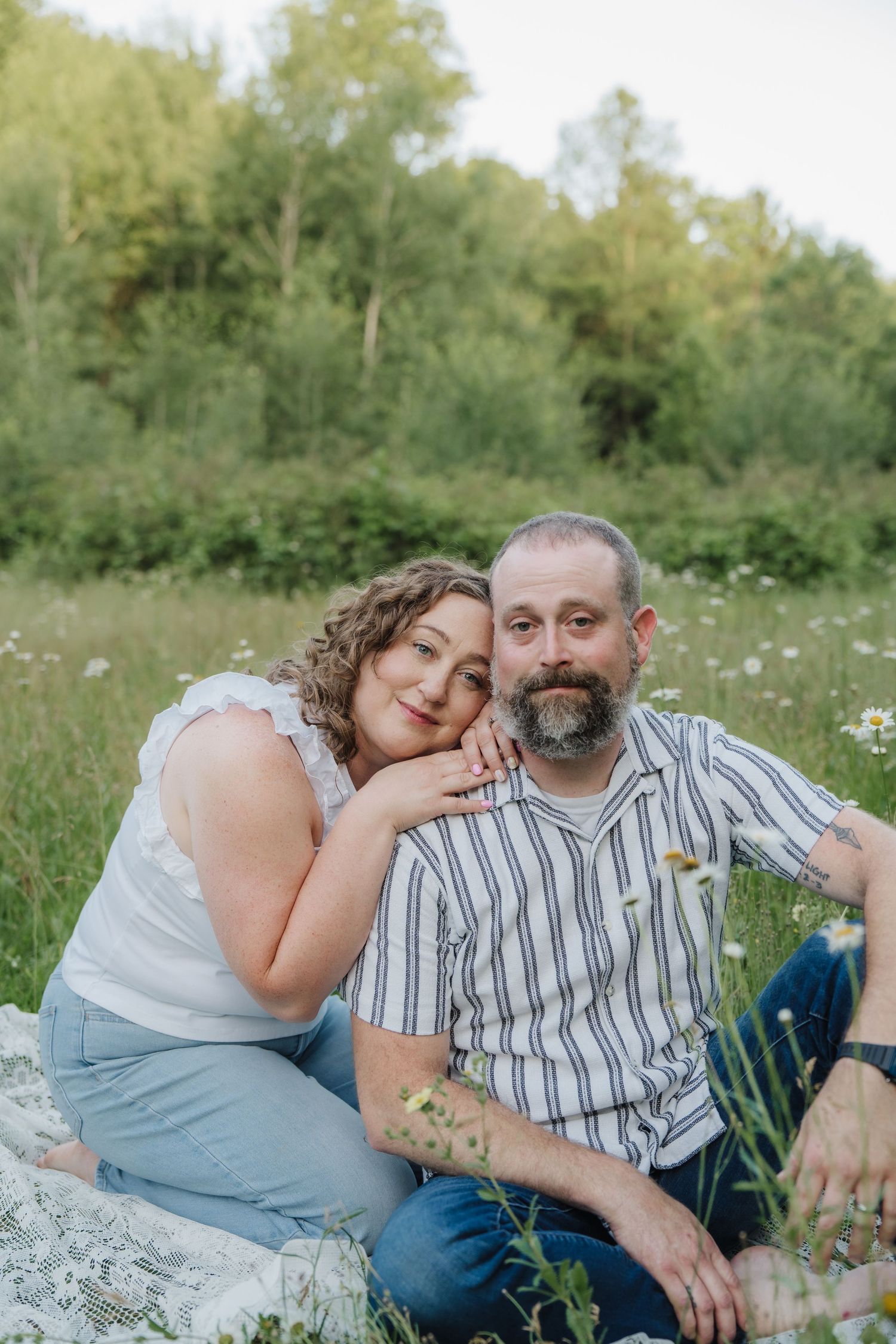 Loving couple sitting together on a blanket in a wildflower meadow, woman resting her head on mans shoulder.