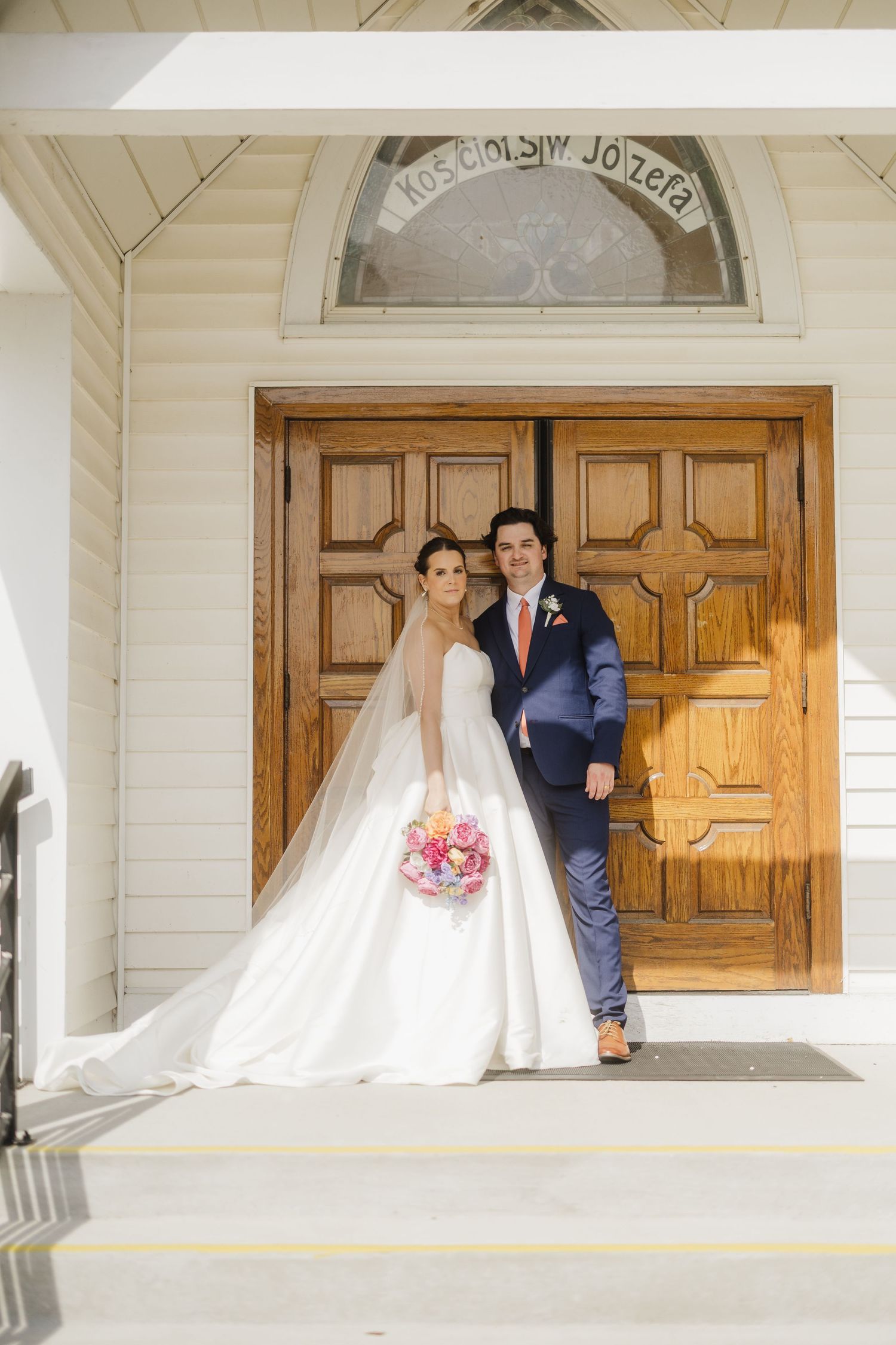 A wedding couple poses in front of elegant wooden church doors for a series of romantic photos.