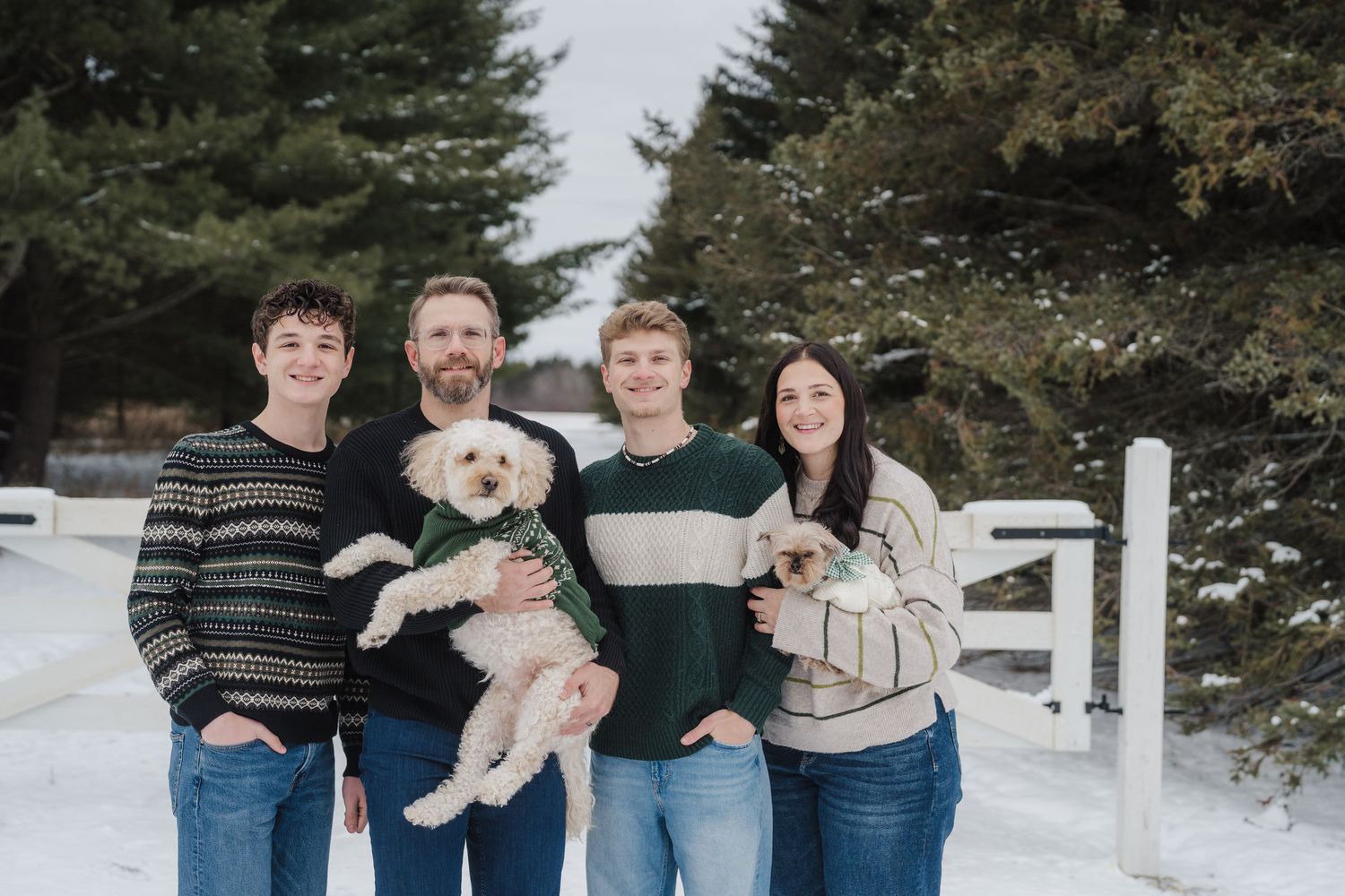 A group poses together outdoors in a snowy winter setting with evergreen trees in the background.