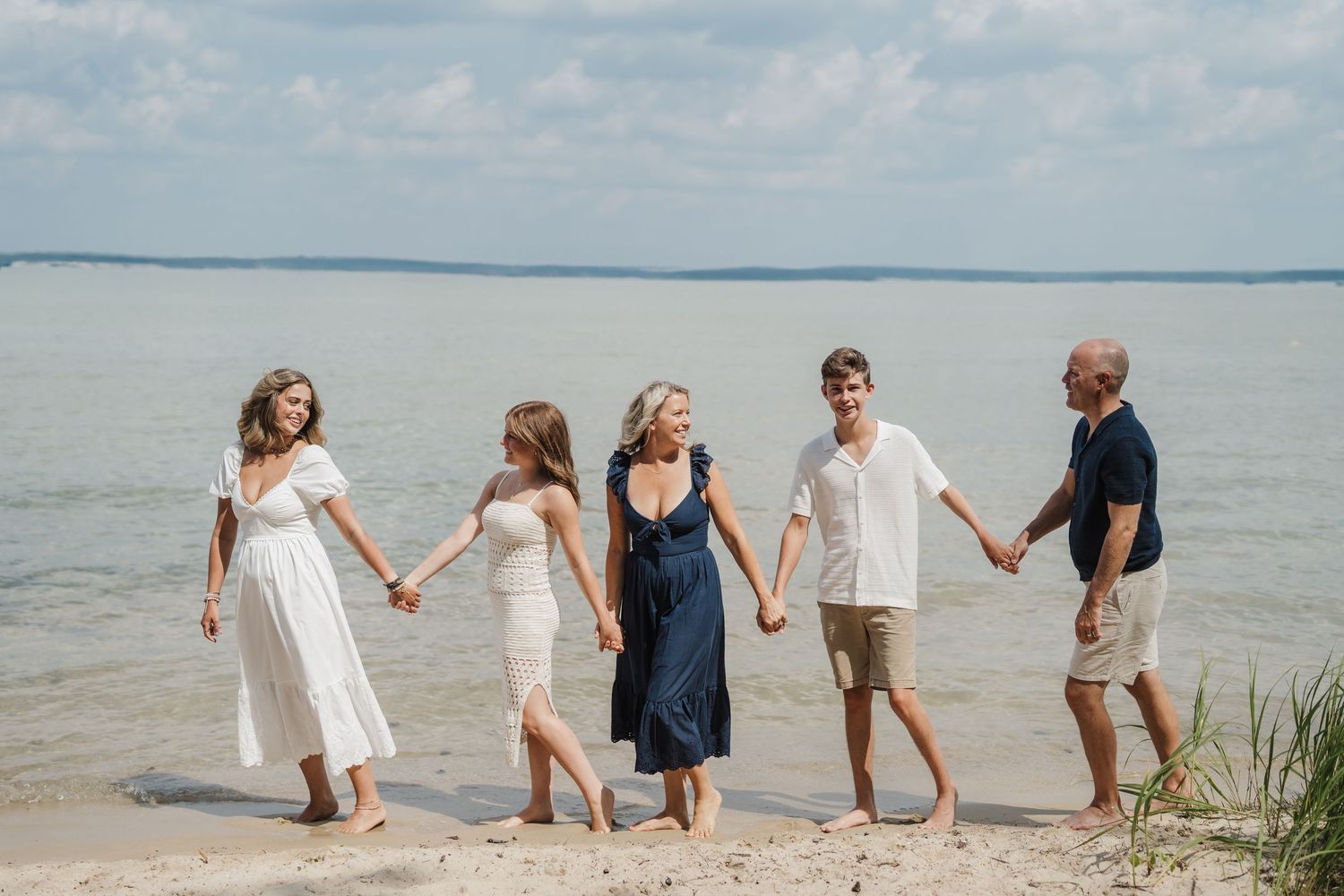 Group of people holding hands while walking along a sandy beach shoreline during a sunny day.