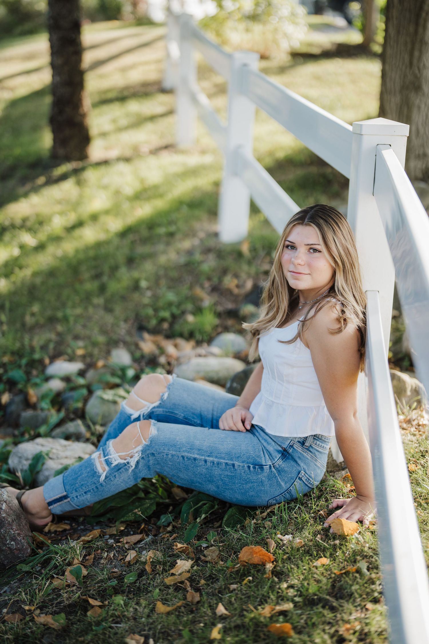 Artistic outdoor portrait session in autumn with white fence and fallen leaves creating a dreamy atmosphere.
