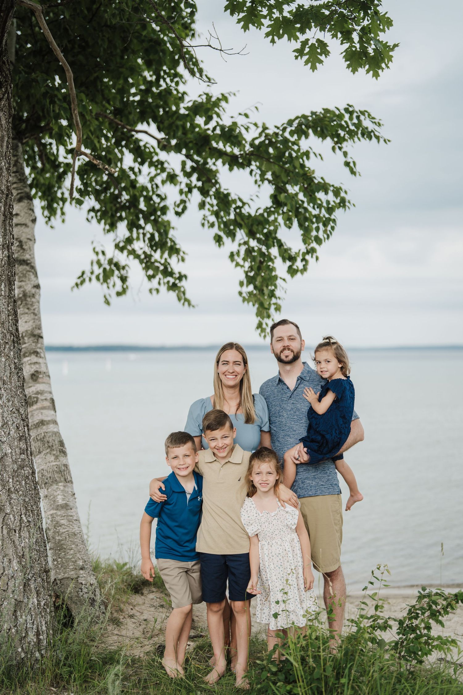 A group poses casually by birch trees near a lake on a cloudy day.