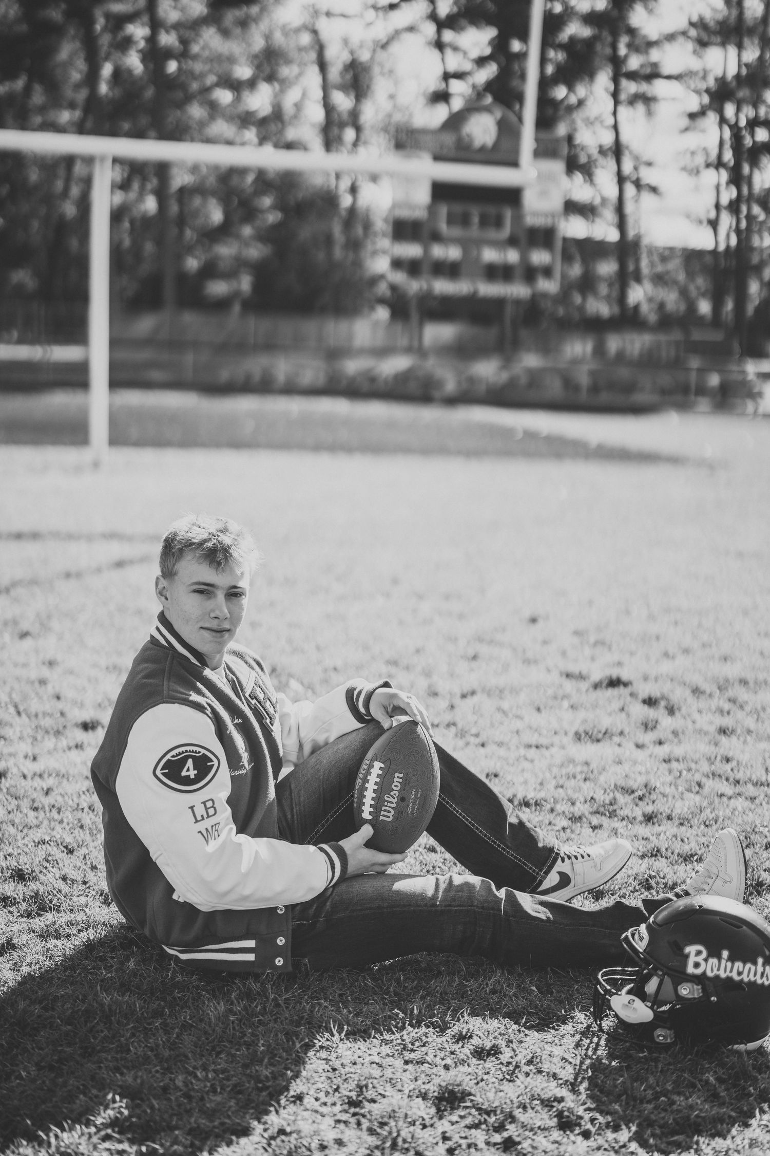 Athletic portraits showing someone in a varsity jacket lying on a football field with a football.
