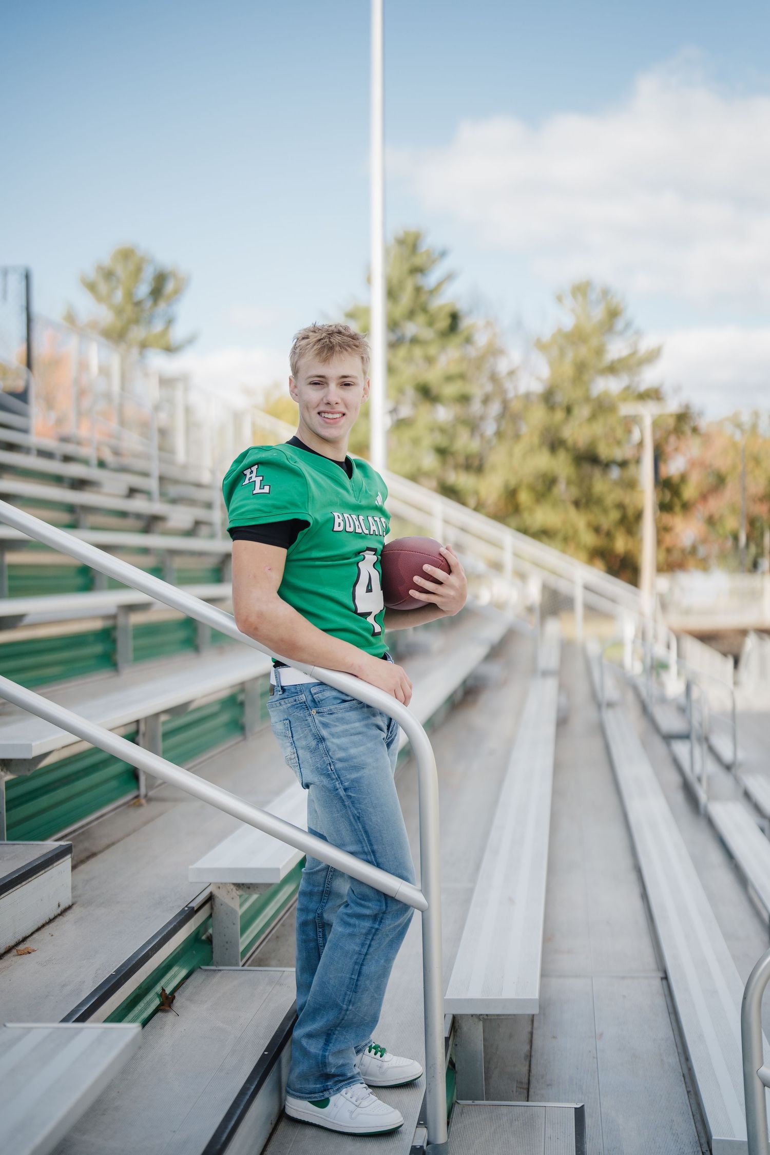 Sports-themed senior portrait session on metal bleachers at an outdoor stadium.