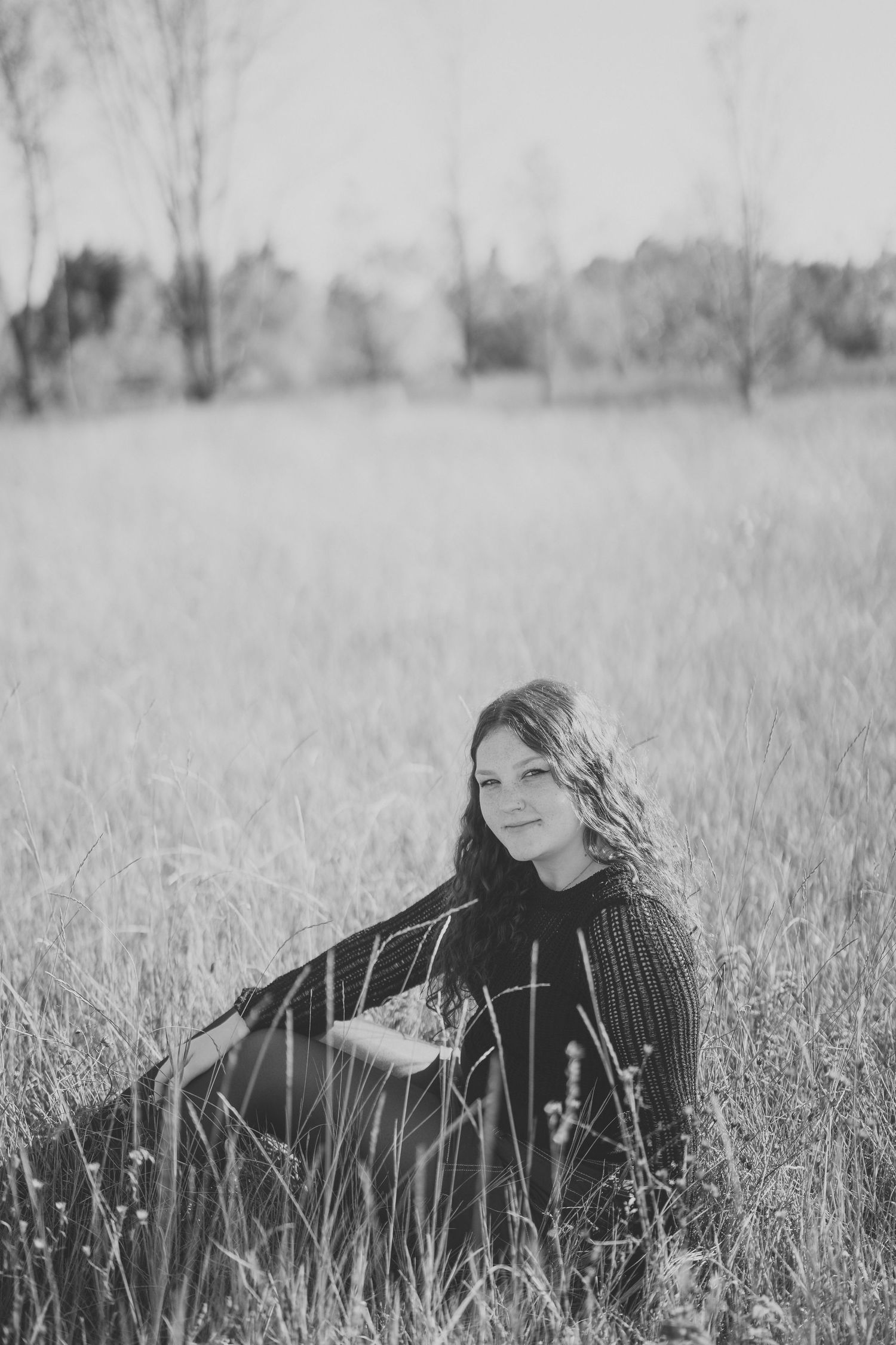 A black and white portrait of someone lying peacefully in tall grass on a sunny day.