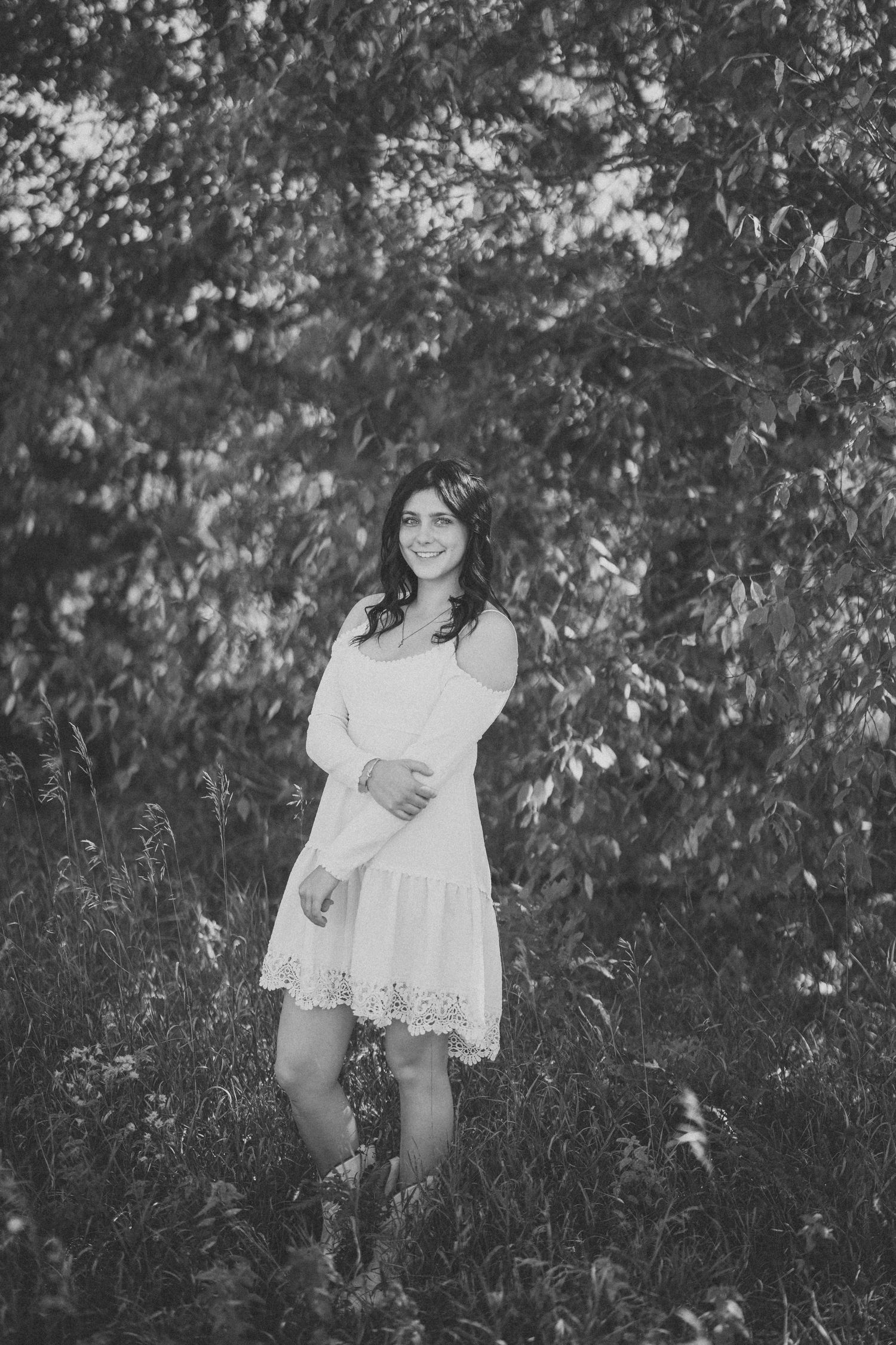 Black and white photo series of a young person in a white lace dress sitting and posing in a natural outdoor setting.