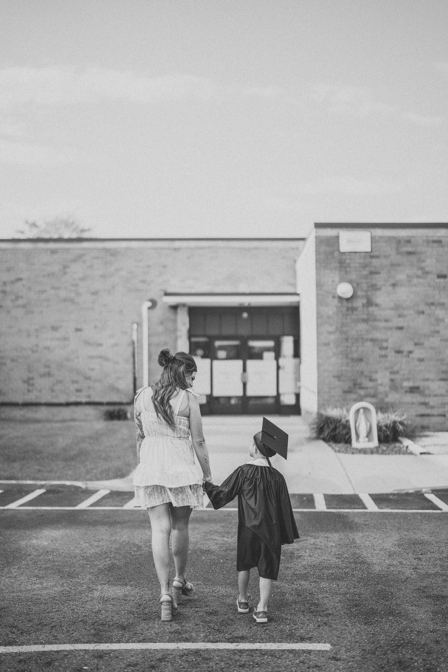 Two small figures walking away on grass in front of a brick building in black and white.
