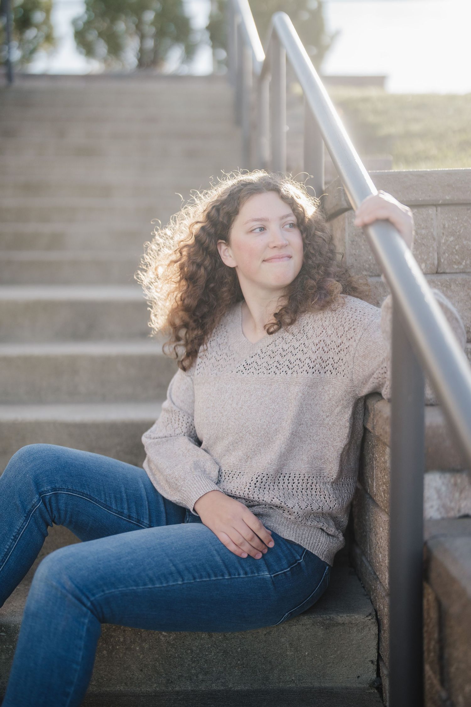 A person in a beige sweater and blue jeans sits casually on concrete steps in a series of outdoor portrait poses.