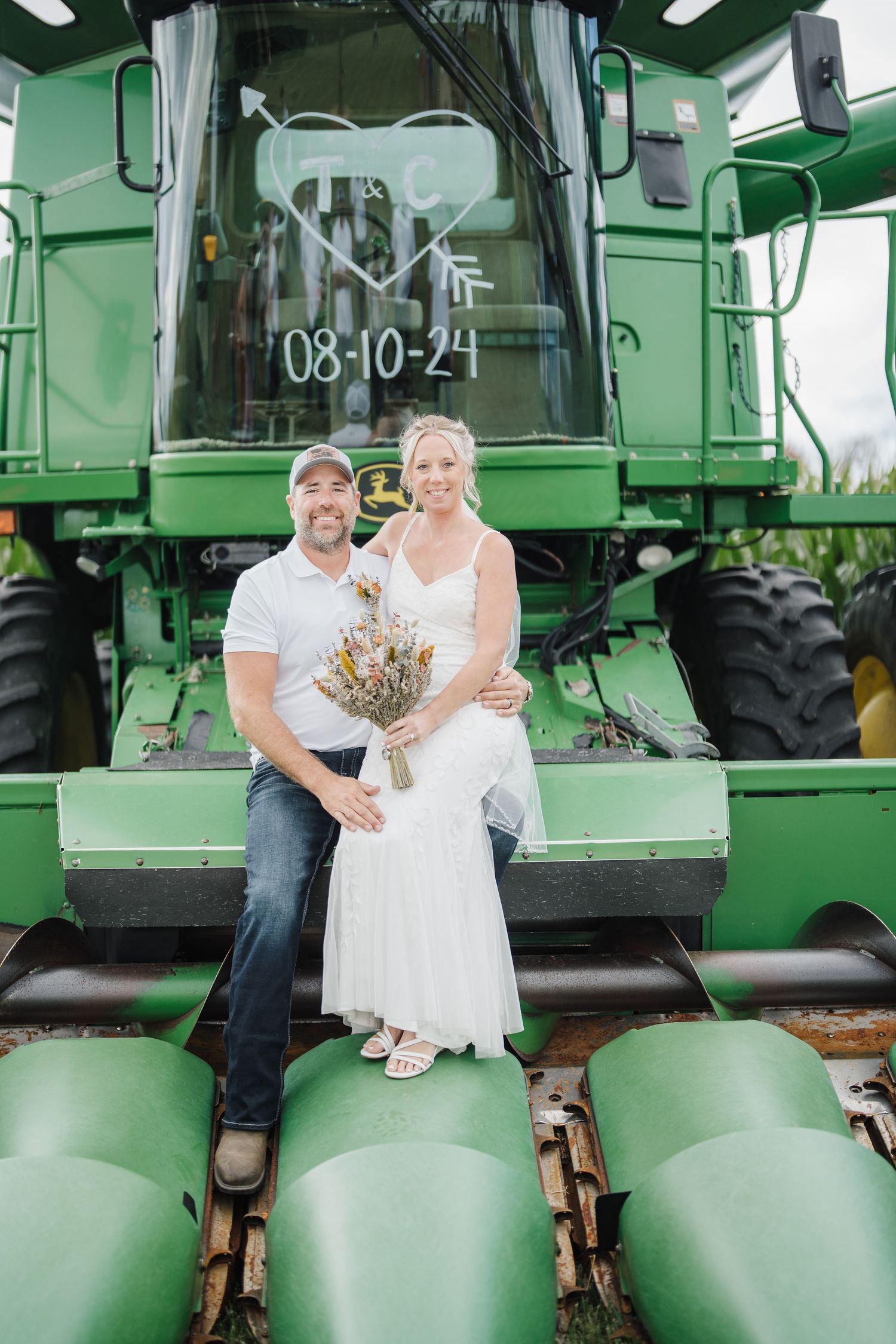 A wedding couple poses on a large green John Deere combine harvester.