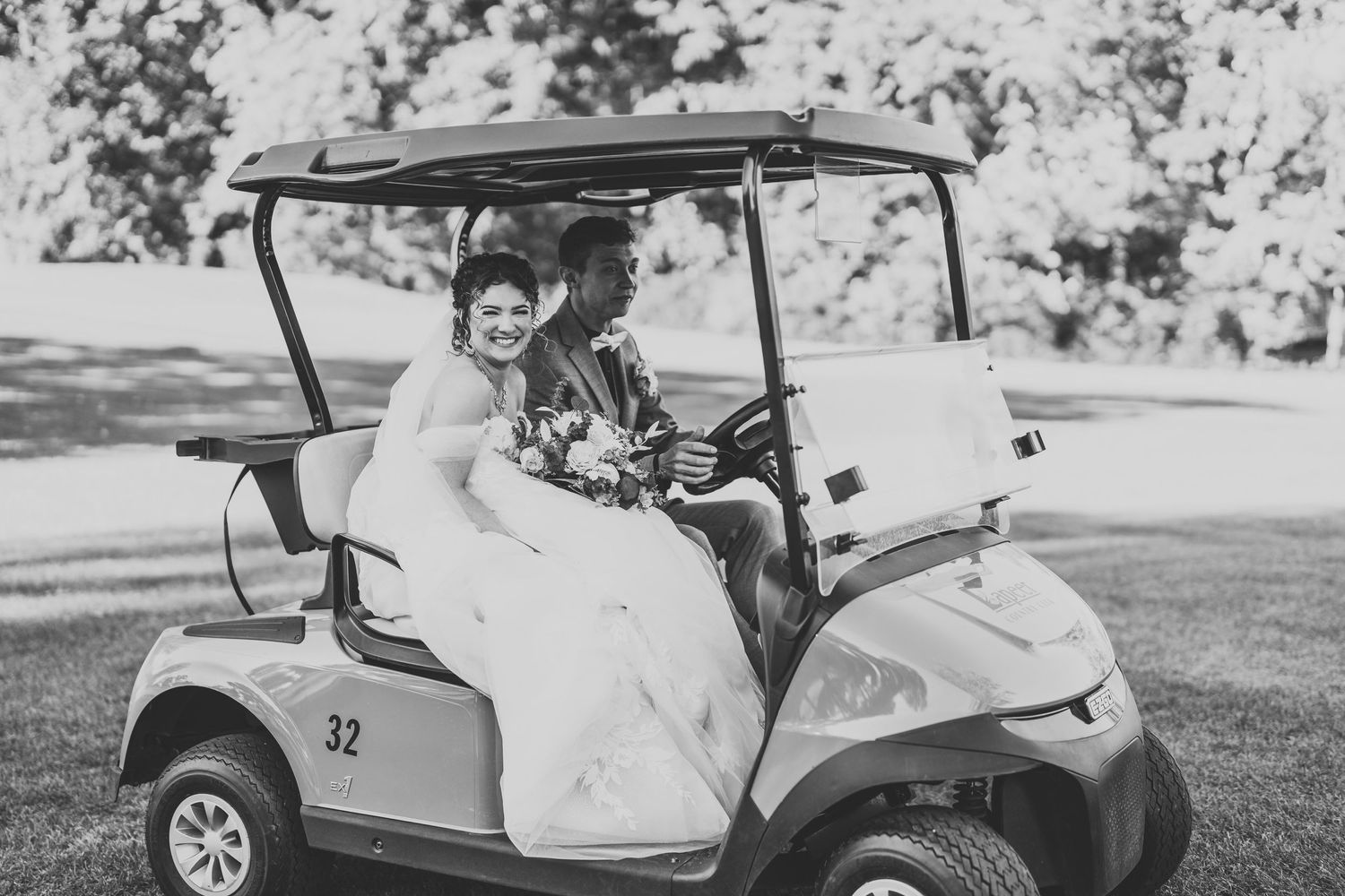 Wedding couple riding in golf cart through scenic grounds in black and white photography.