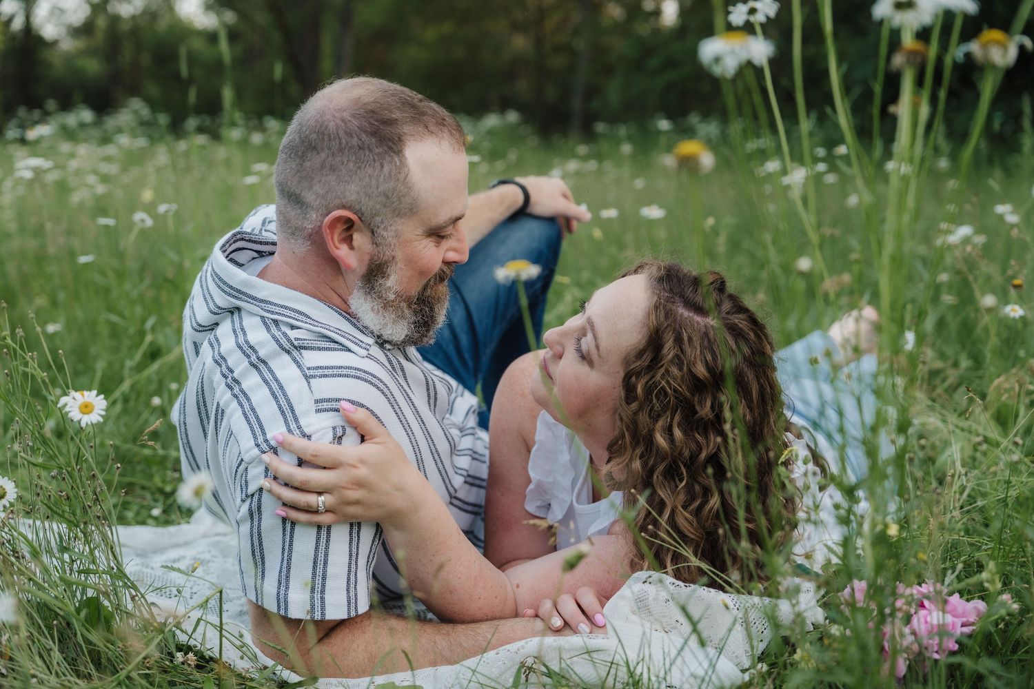 Couple lying in a wildflower meadow, sharing a romantic moment surrounded by daisies and pink blooms.