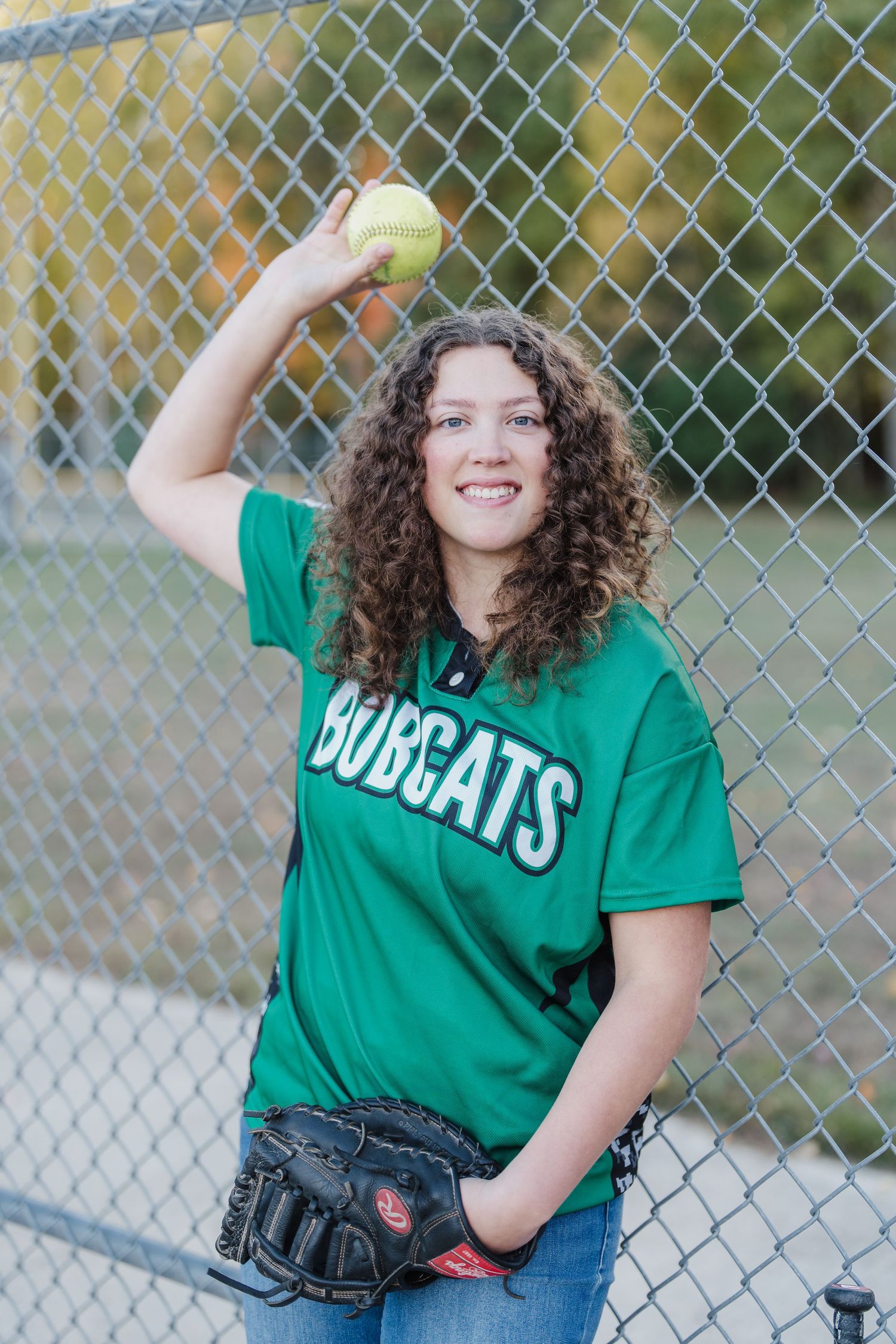 A softball player in a green Bobcats jersey poses against a chain link fence in a series of casual portraits.