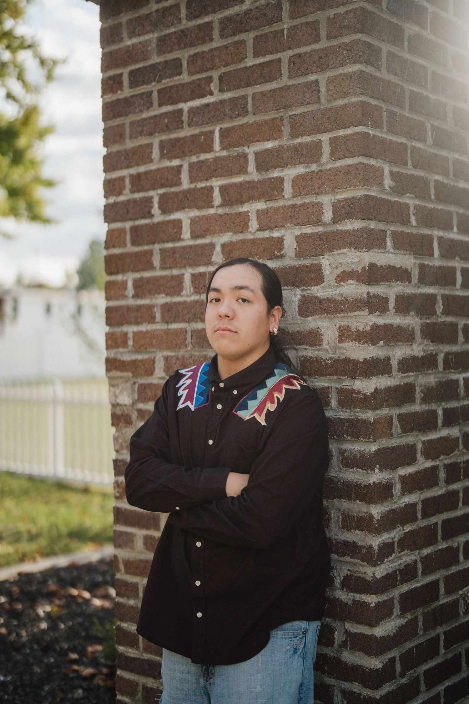 Person wearing black jacket leans against brick wall in outdoor portrait series.