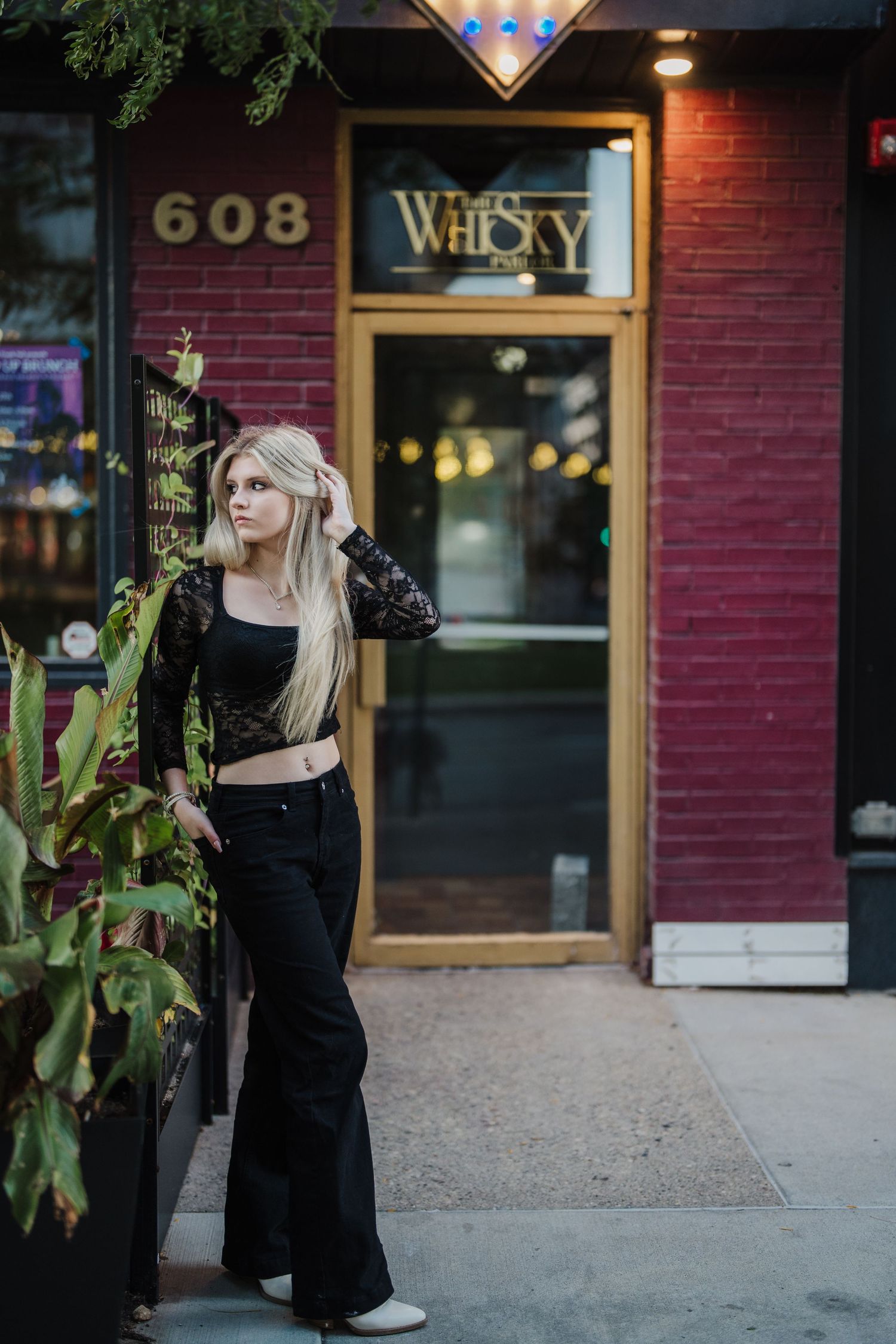 A woman in a black dress poses outside a brick building with a storefront window and address number 608.