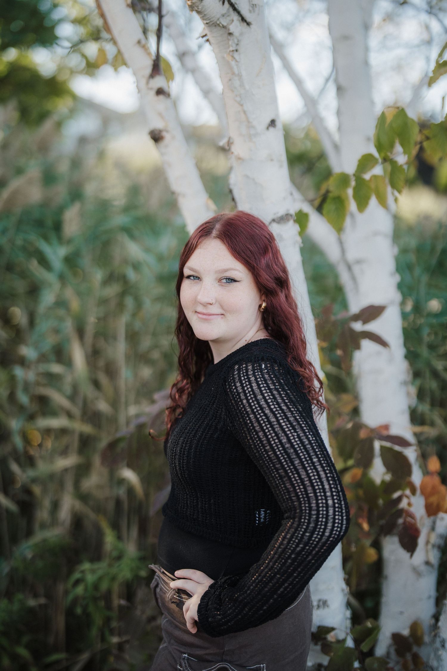 Natural light portrait by white birch trees showcasing a black knit sweater and autumn scenery.