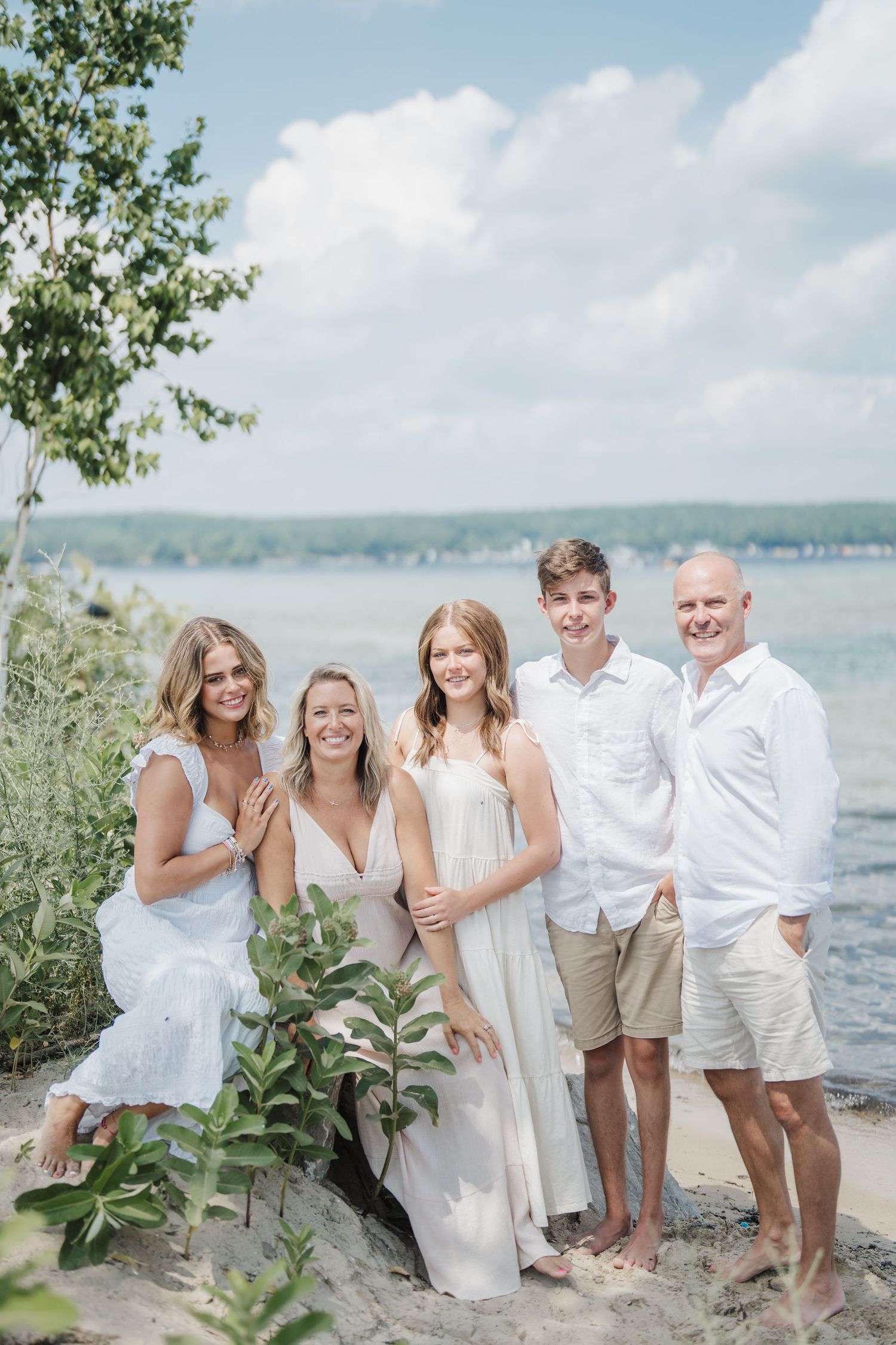 A group in white attire poses together by the waterfront on a sunny summer day.