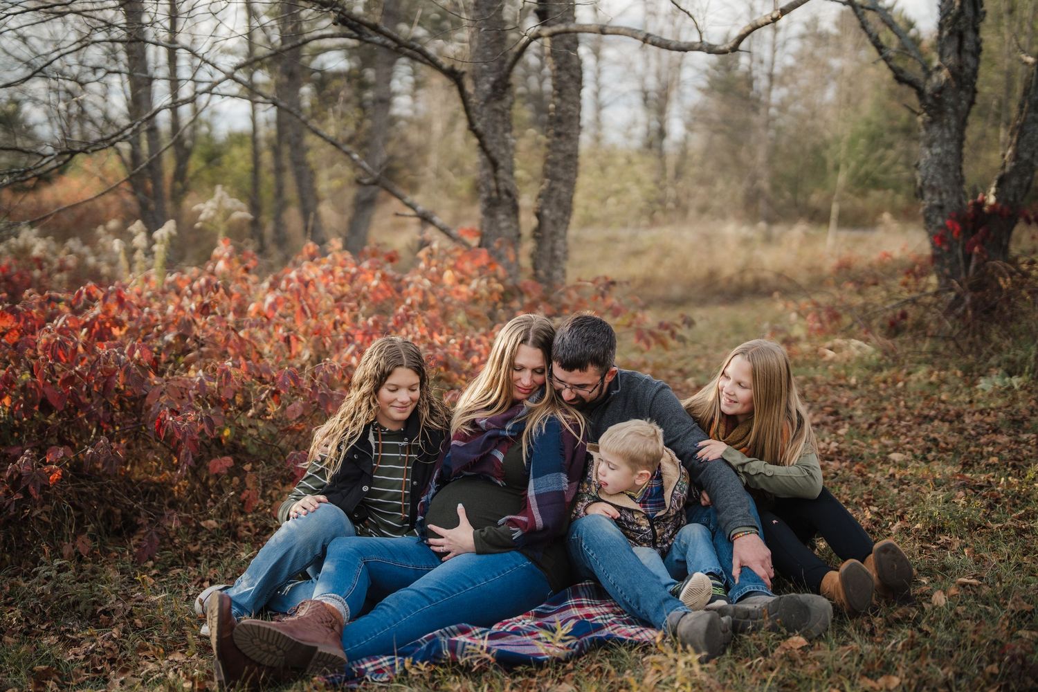 A group relaxes on a cozy blanket during an autumn photoshoot in a wooded park setting.