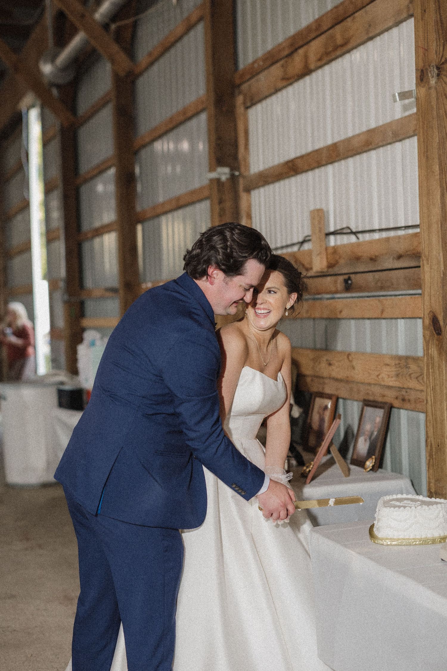 A couple shares an intimate moment while cutting their wedding cake together in a rustic barn setting.