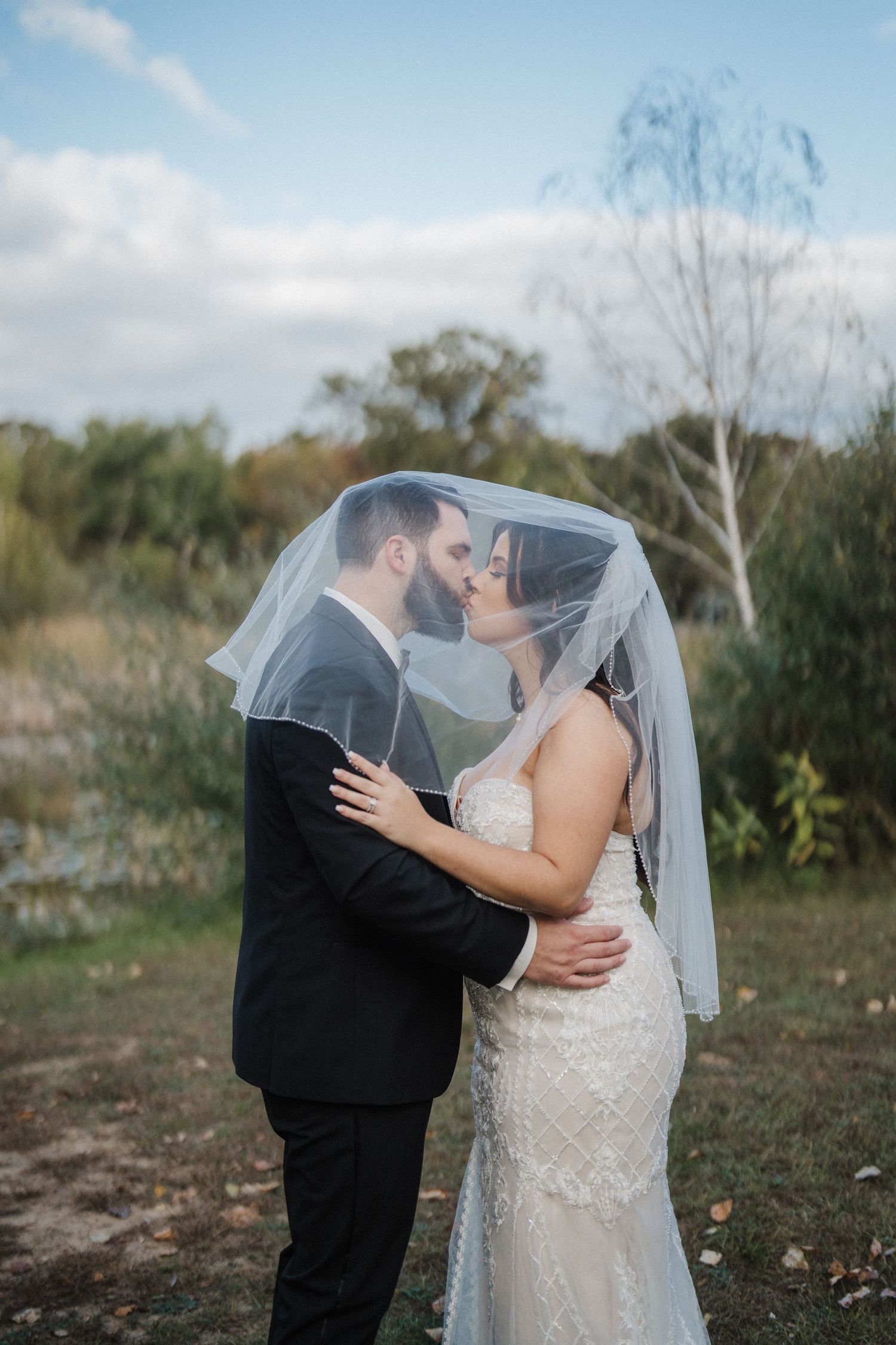 Romantic wedding couple shares intimate moments in an outdoor autumn setting with flowing veil.