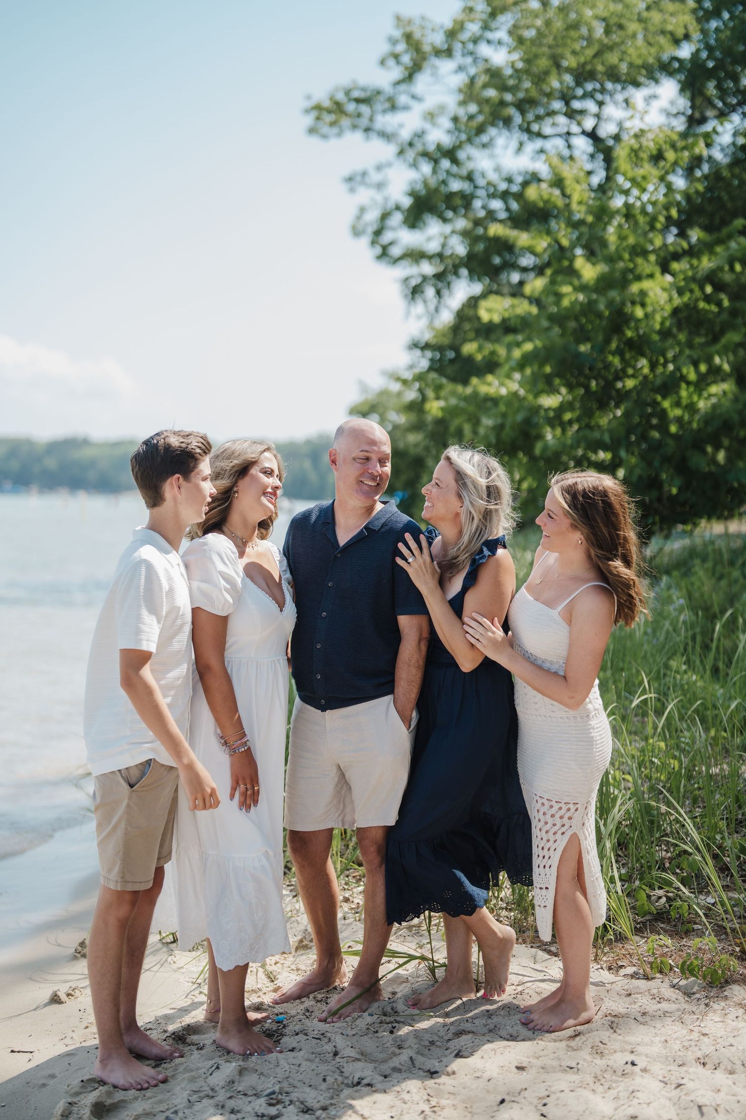 A group of people standing together on a sandy beach wearing white and navy outfits near the water's edge.