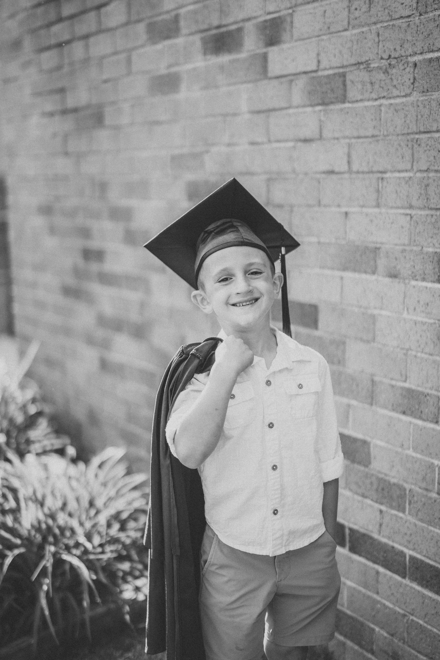 A young child in formal attire poses playfully against a brick wall in a series of black and white portraits.