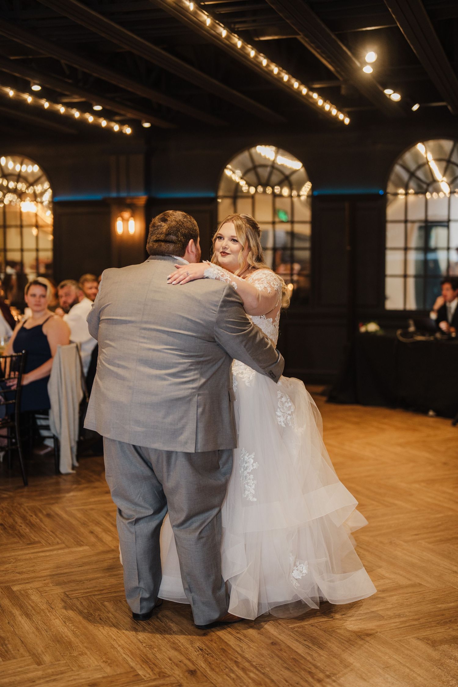 Wedding couple shares first dance under string lights in elegant reception venue.