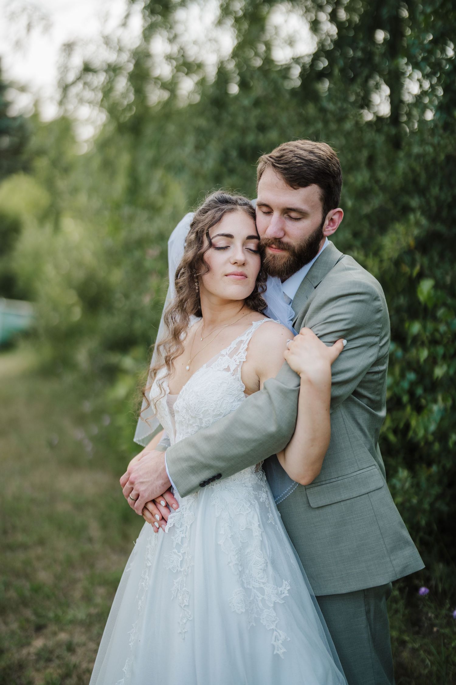 Intimate moment between newlyweds embracing outdoors with soft natural lighting.