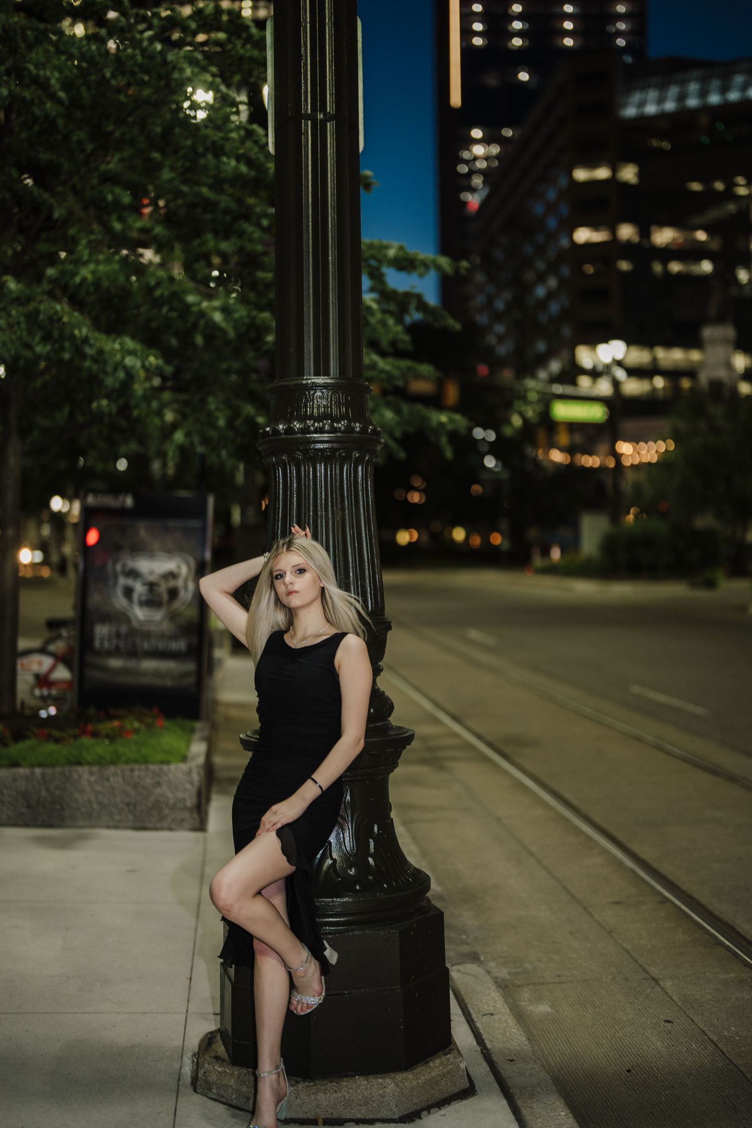 Artistic portrait series of a figure in black dress posing against an ornate lamp post at dusk in an urban setting.