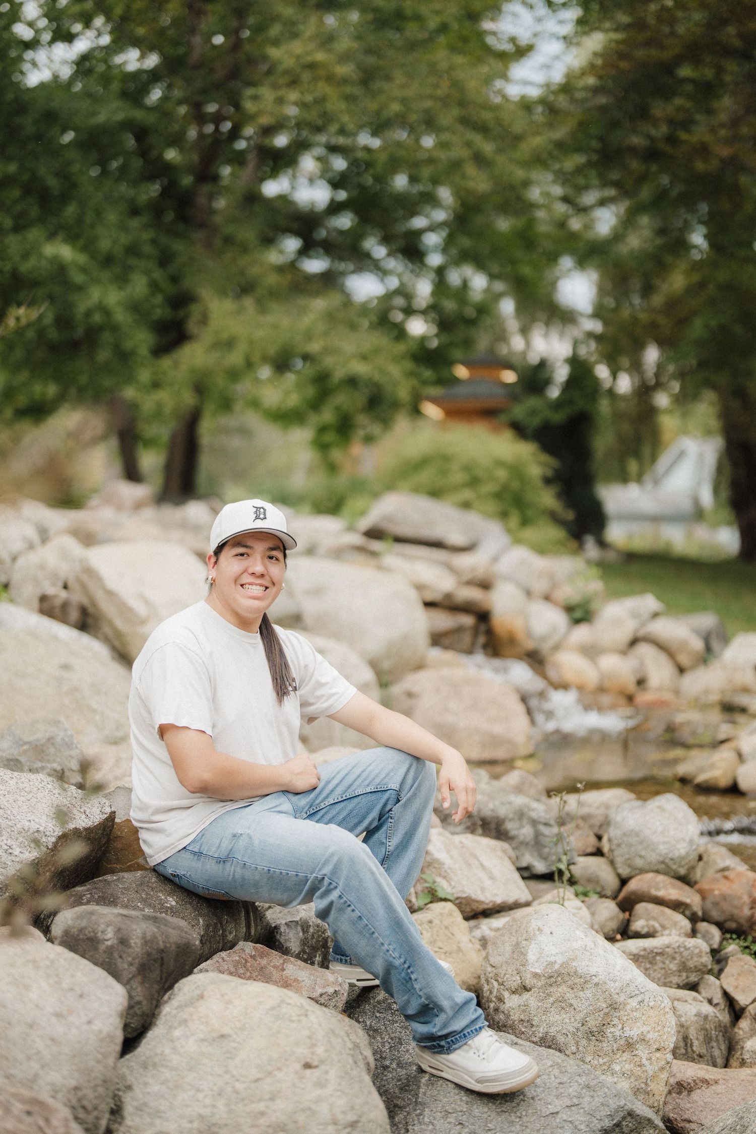 Person in white shirt and jeans sits casually on rocky terrain outdoors.