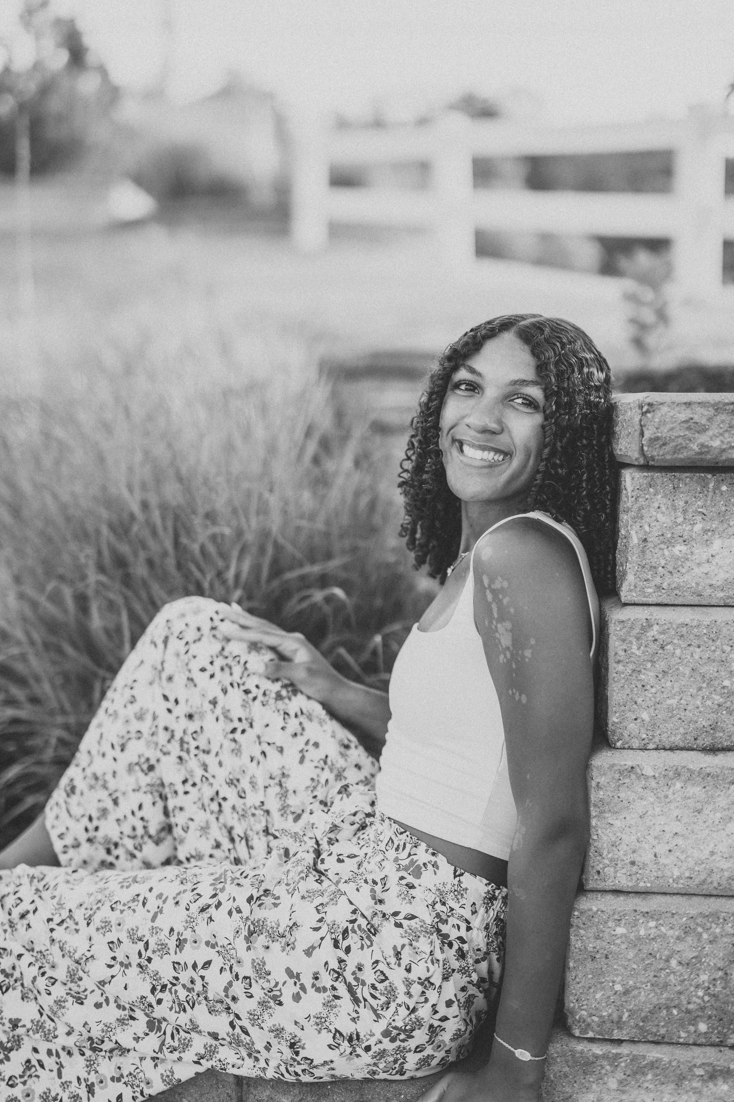 A black and white portrait of someone in summer attire sitting on stone steps with ornamental grasses.