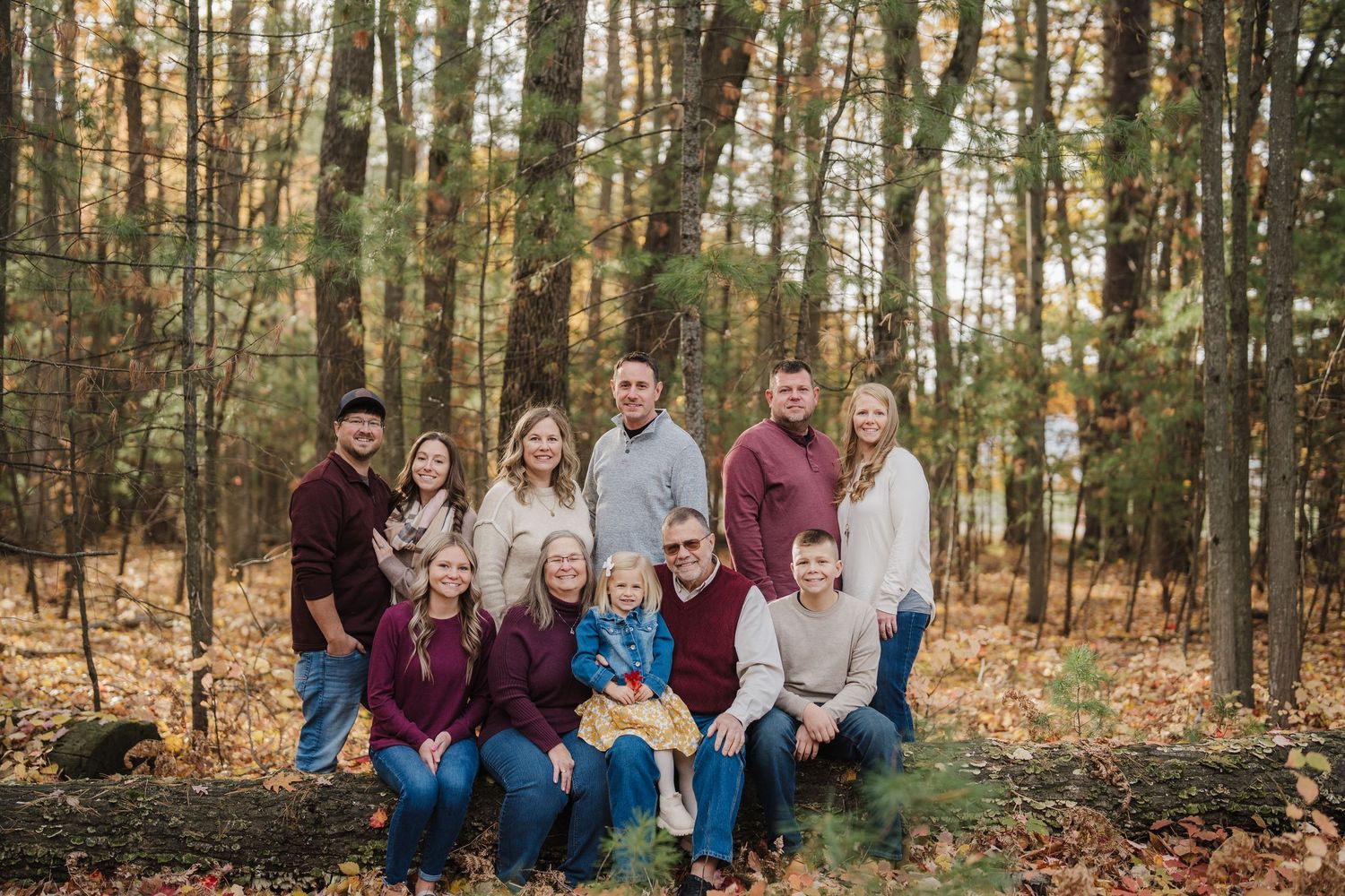 A group of people in coordinating burgundy and neutral outfits pose together in an autumn forest setting.