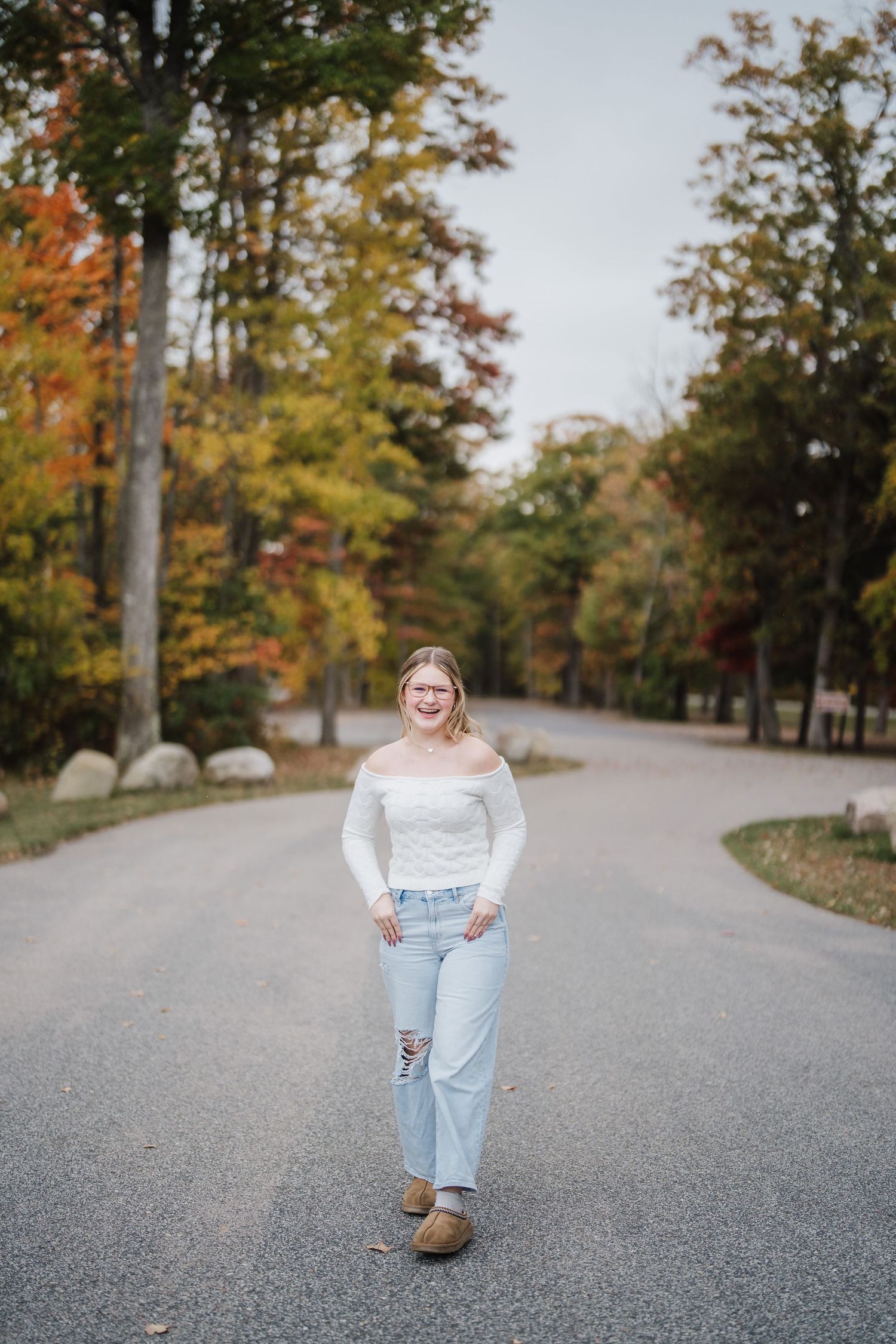 A person stands on a winding autumn road surrounded by trees with colorful fall foliage.