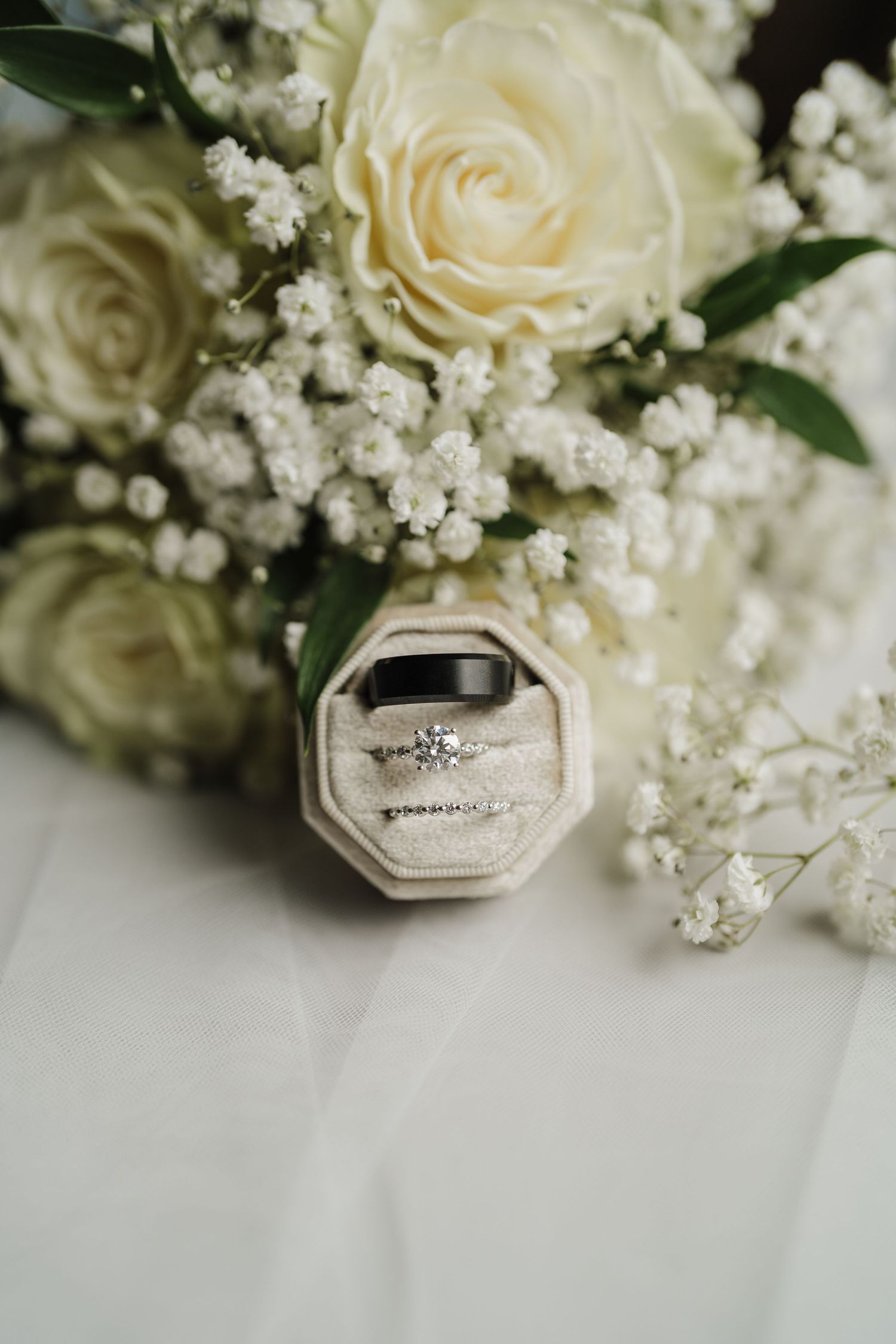 Elegant white roses and baby's breath flowers arranged with vintage-style ring boxes on a light background.
