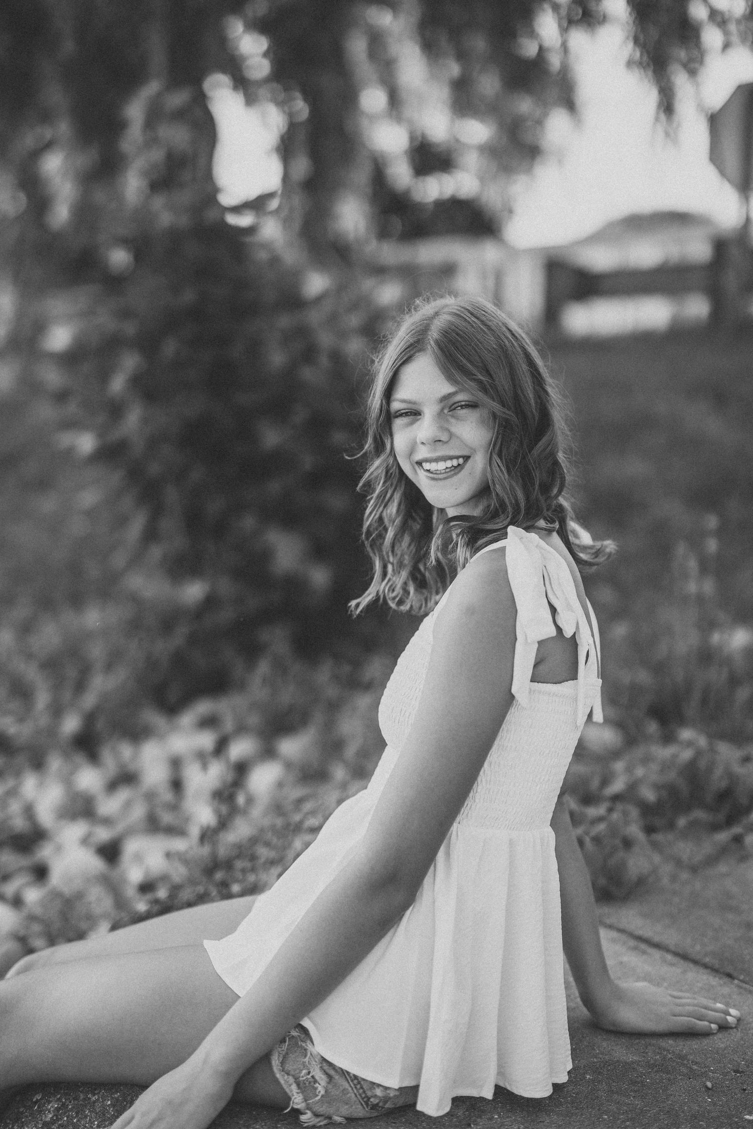 A black and white photo series shows a person in a white dress sitting and laughing joyfully in an outdoor setting.
