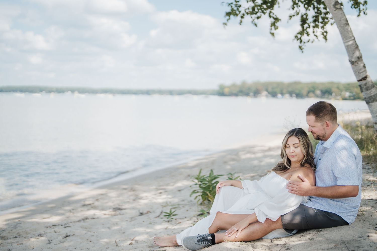 Romantic couple lounges together on a sandy beach with ocean waves and trees in the background.