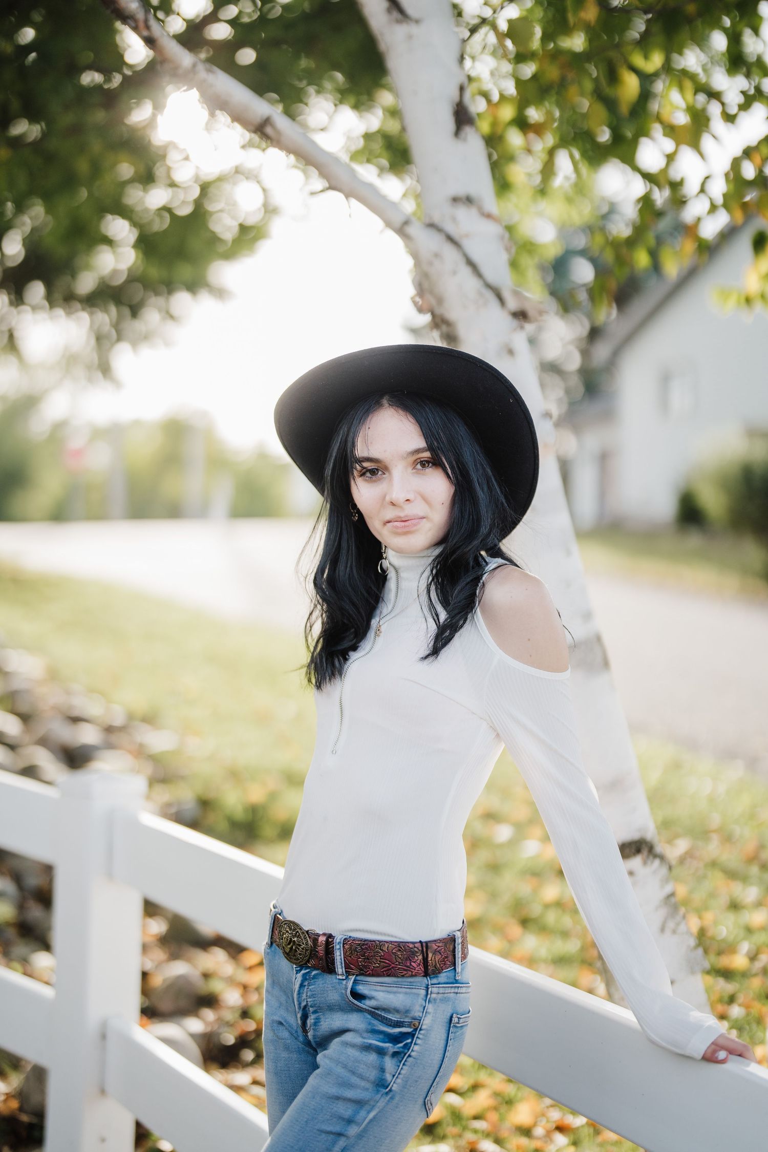 A person in a white sweater and jeans poses outdoors near white birch trees on an autumn day.