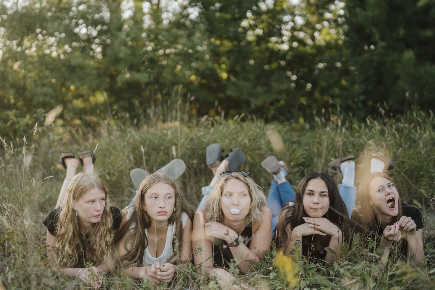 A group of people lying in a row on grass outdoors during a sunny day.