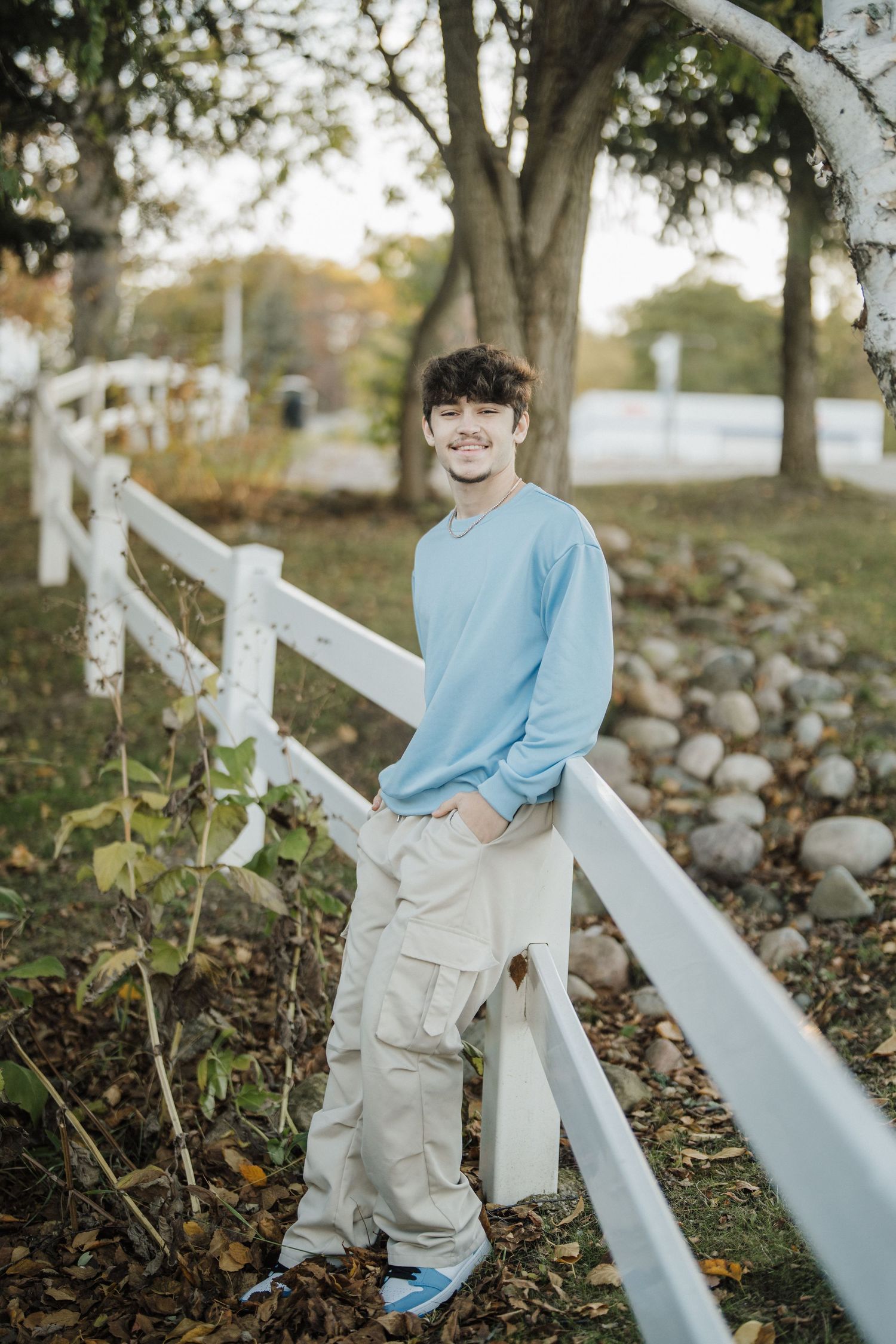 A relaxed outdoor photo shoot featuring white fencing and autumn foliage in the background.