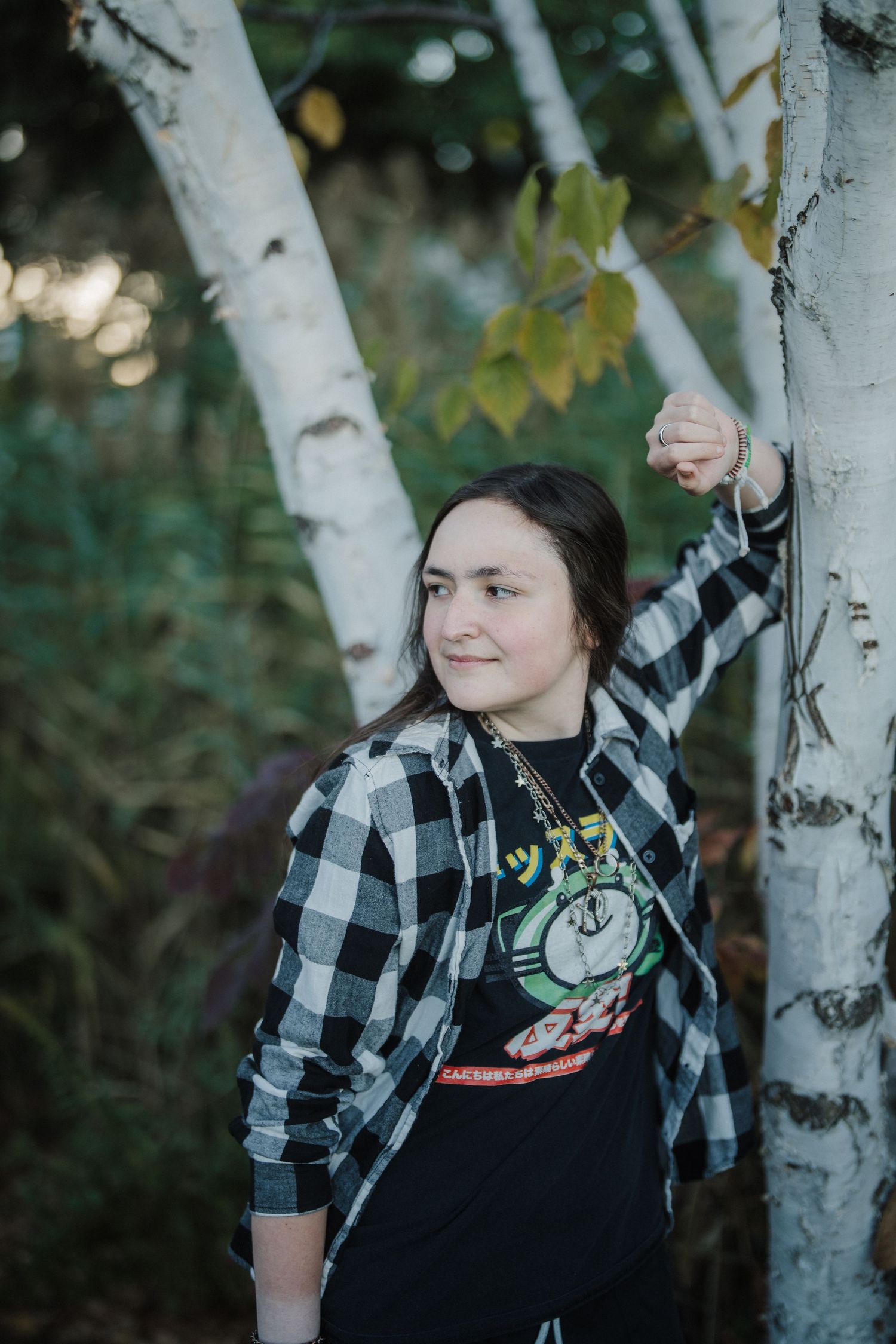 A person in a black and white plaid flannel shirt poses near white birch trees in an outdoor setting.