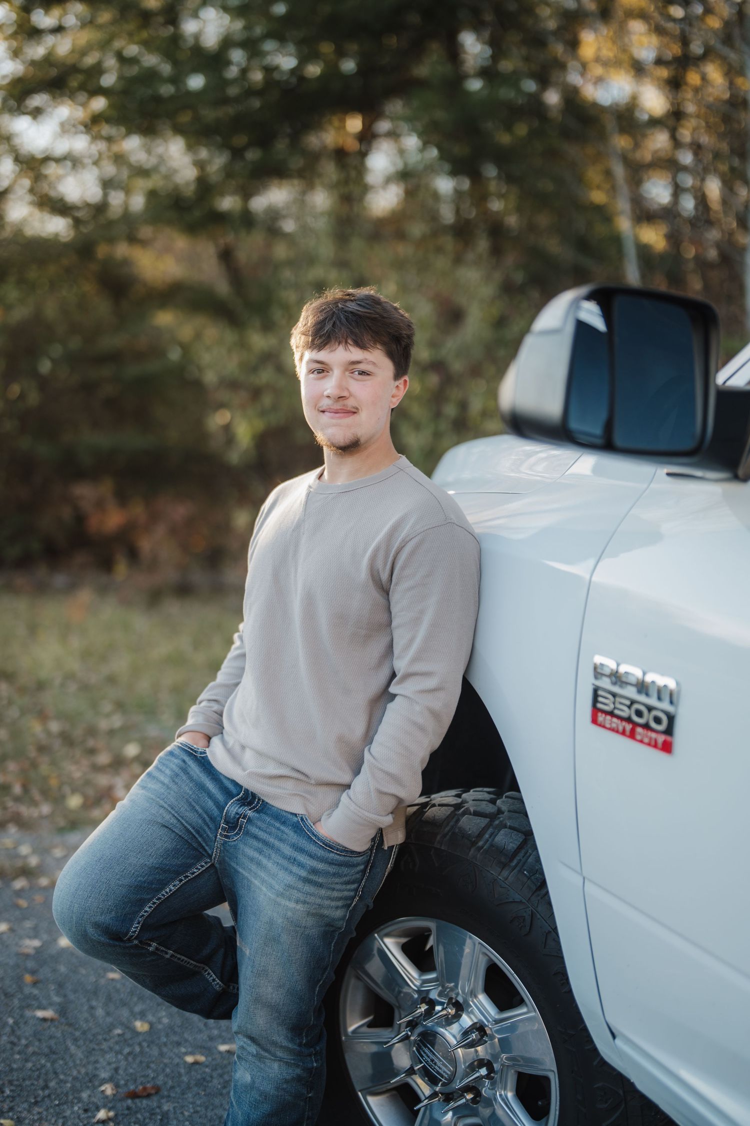A person in a gray sweater and jeans sits casually on the side of a white pickup truck in an outdoor setting.