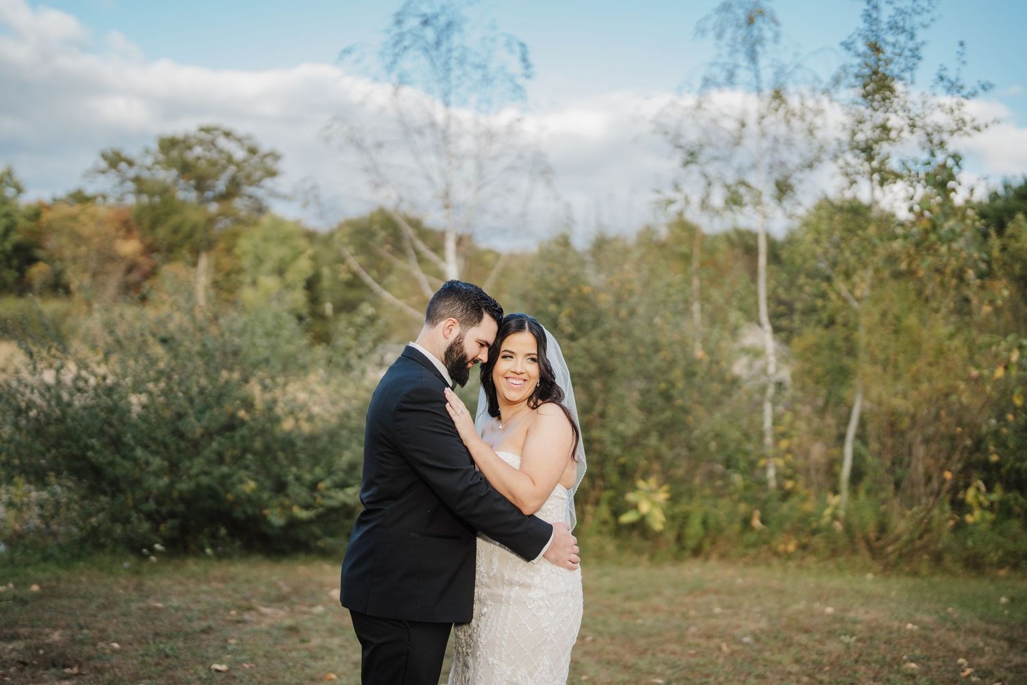 A couple in wedding attire shares romantic moments in a scenic outdoor setting with lush greenery and natural lighting.