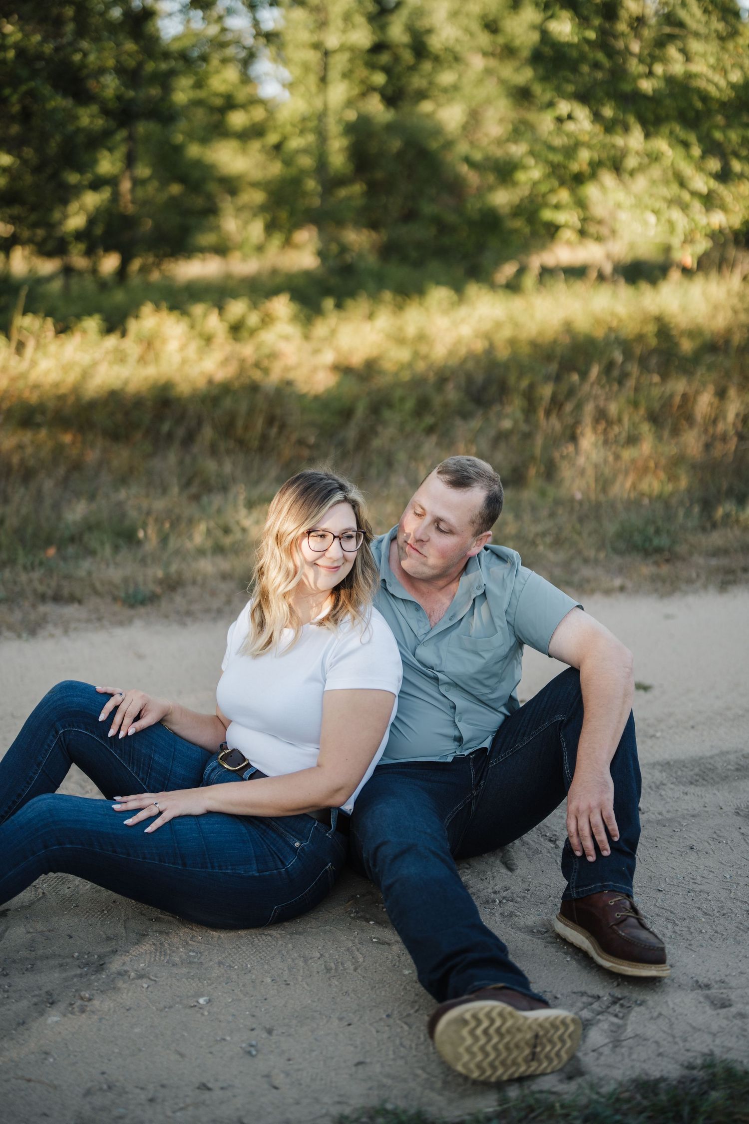 A couple relaxes together on a sandy beach path during golden hour, sharing intimate moments in casual attire.
