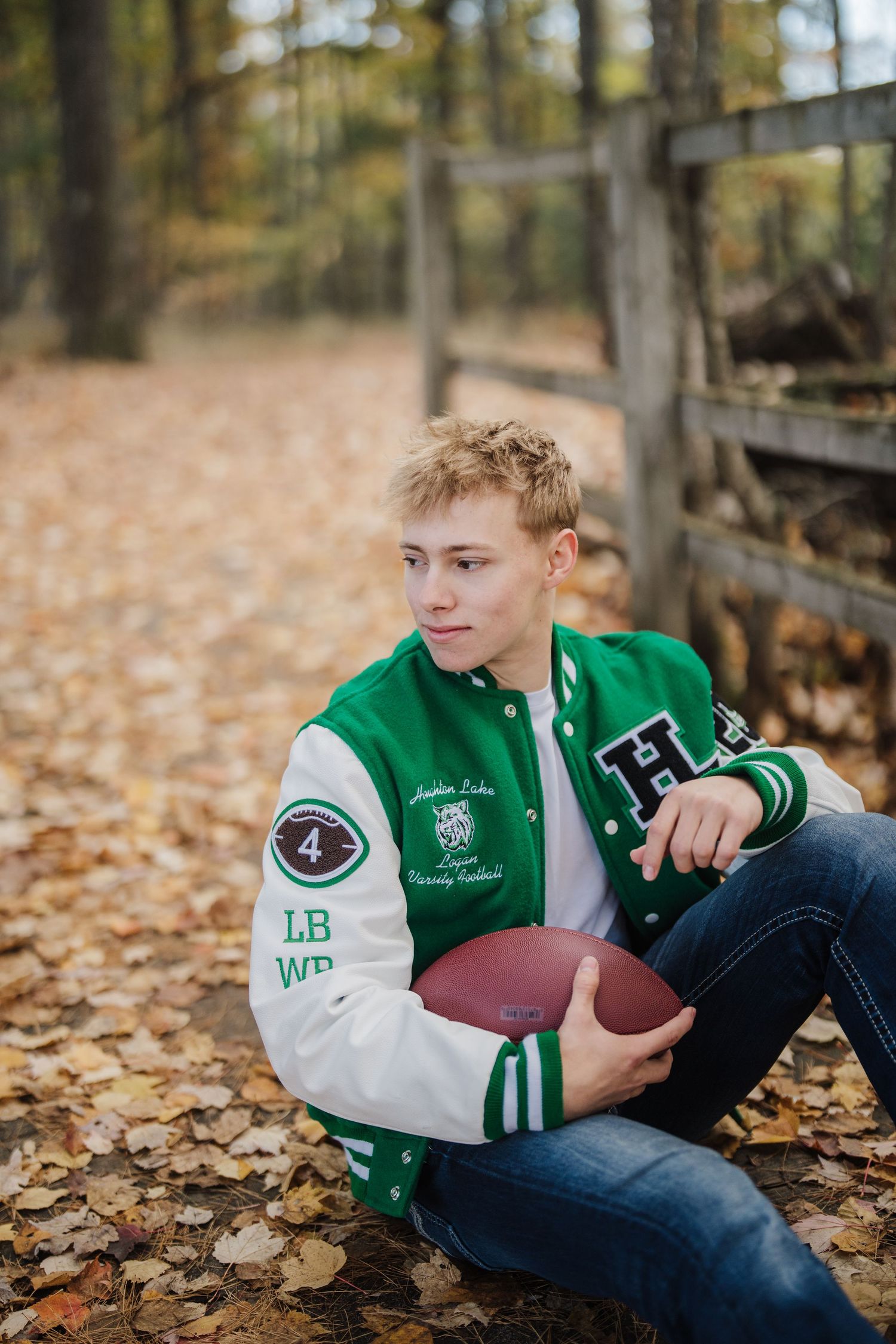 A varsity letterman jacket photo session with a football prop among fallen autumn leaves.