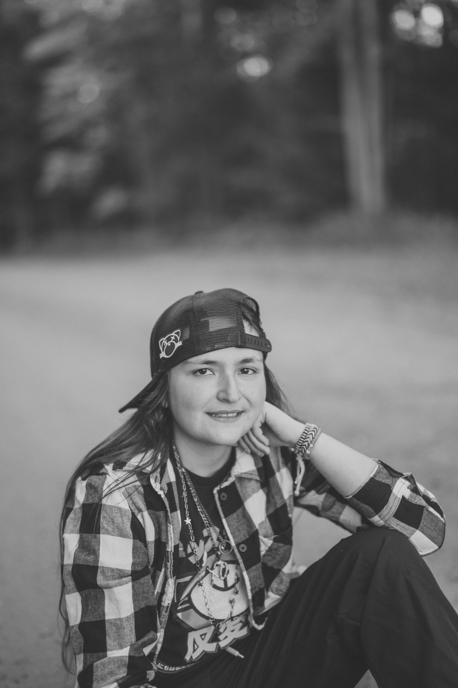 A person in a plaid shirt and baseball cap poses outdoors in a casual black and white portrait series.