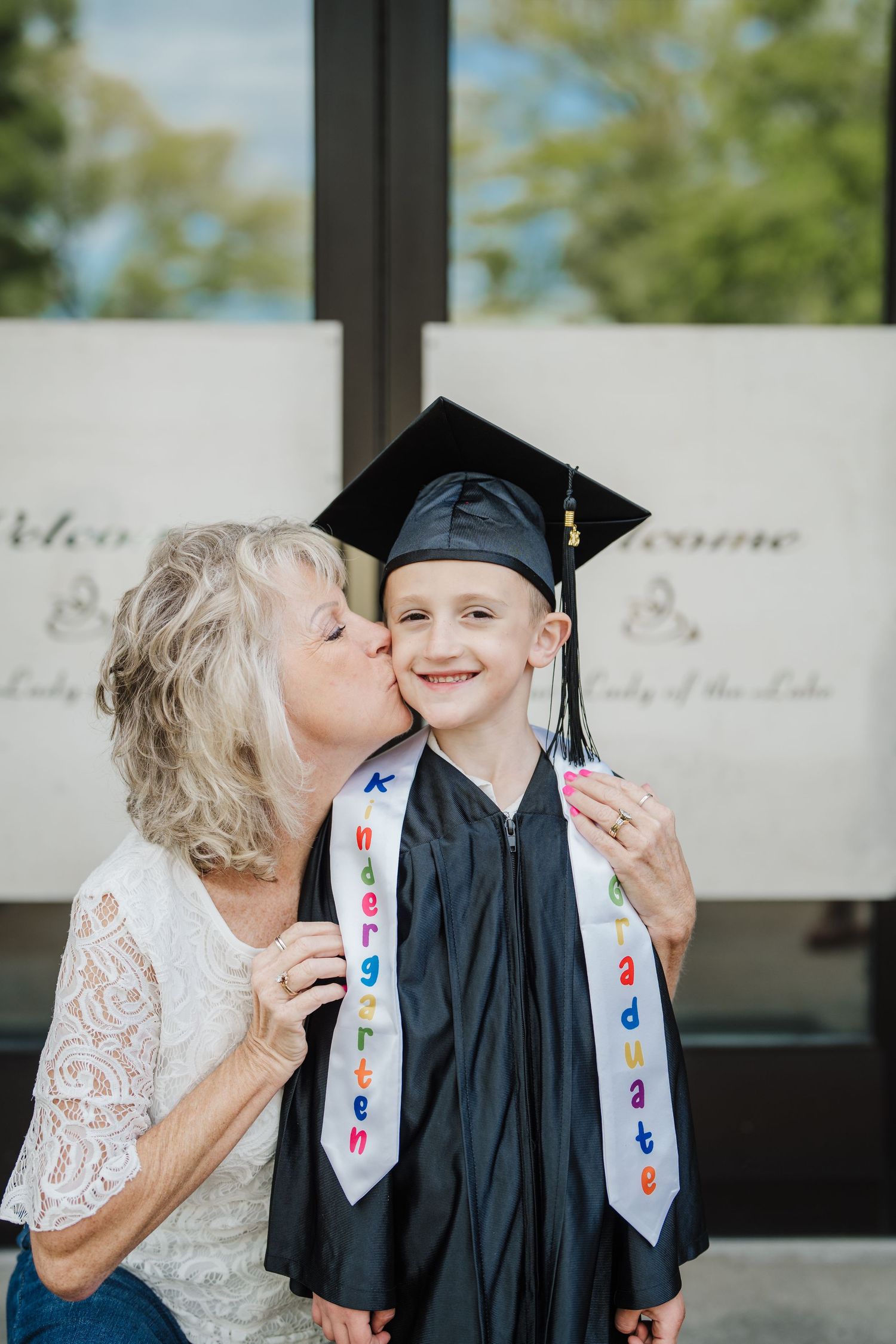 A person in a white lace dress and graduation stole shares a tender moment with someone in a black graduation gown.