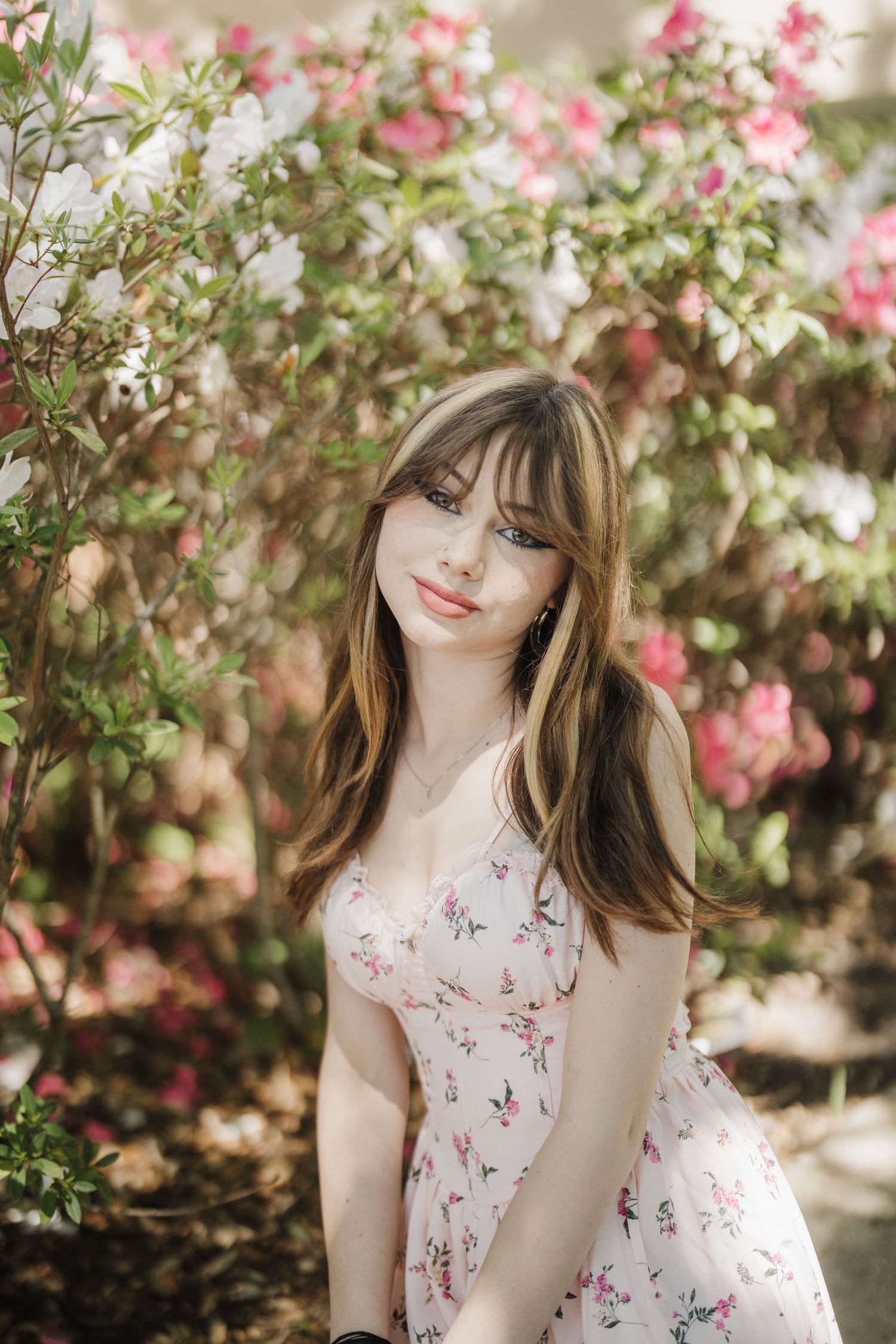 Soft sunlight filters through trees onto a floral dress amid pink blooming flowers in a lush garden.