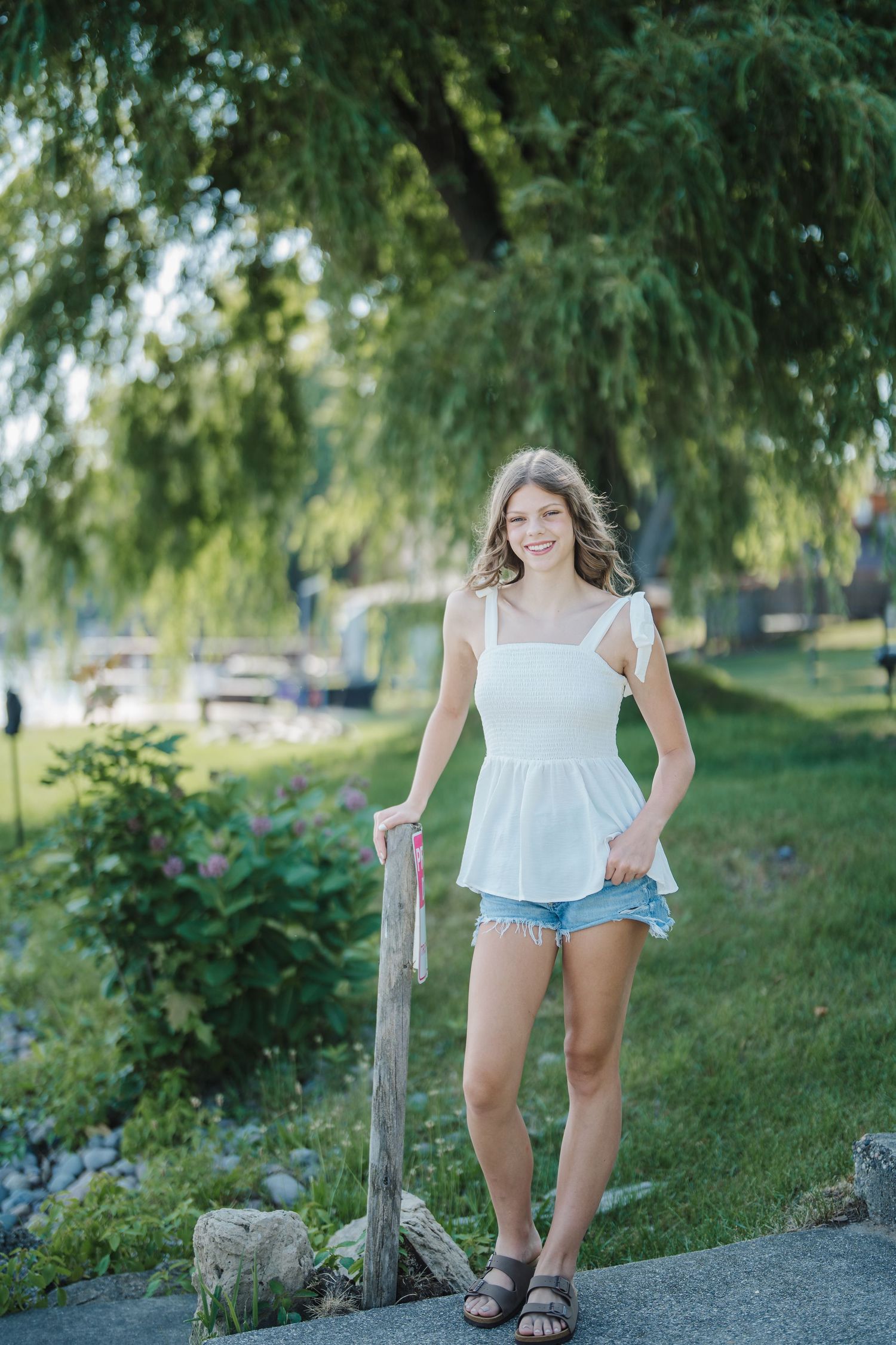 A series of four photos showing someone in a white top and denim shorts posing casually outdoors near trees and a fence post.