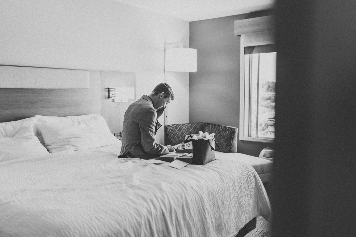 Person sitting on hotel bed looking at laptop in black and white photography.